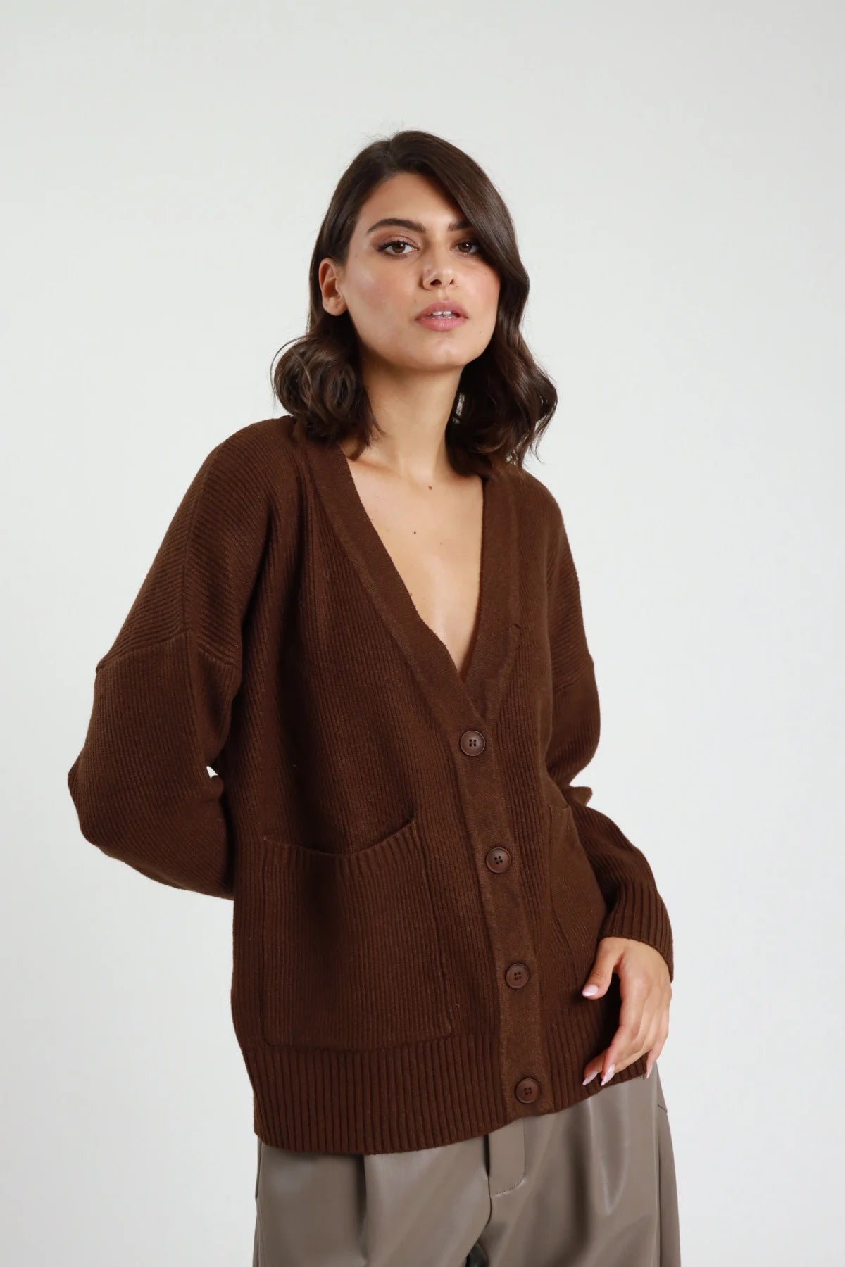 Cardigan over maglia coste spesse scollo V abbottonatura 5 bottoni tono su tono batwing oversize 2 tasche patch grigio melange frontale busto mano spalla - modella frontale busto mano spalla sguardo frontale capelli castani lisci sfondo bianco pantaloni bordeaux in pelle