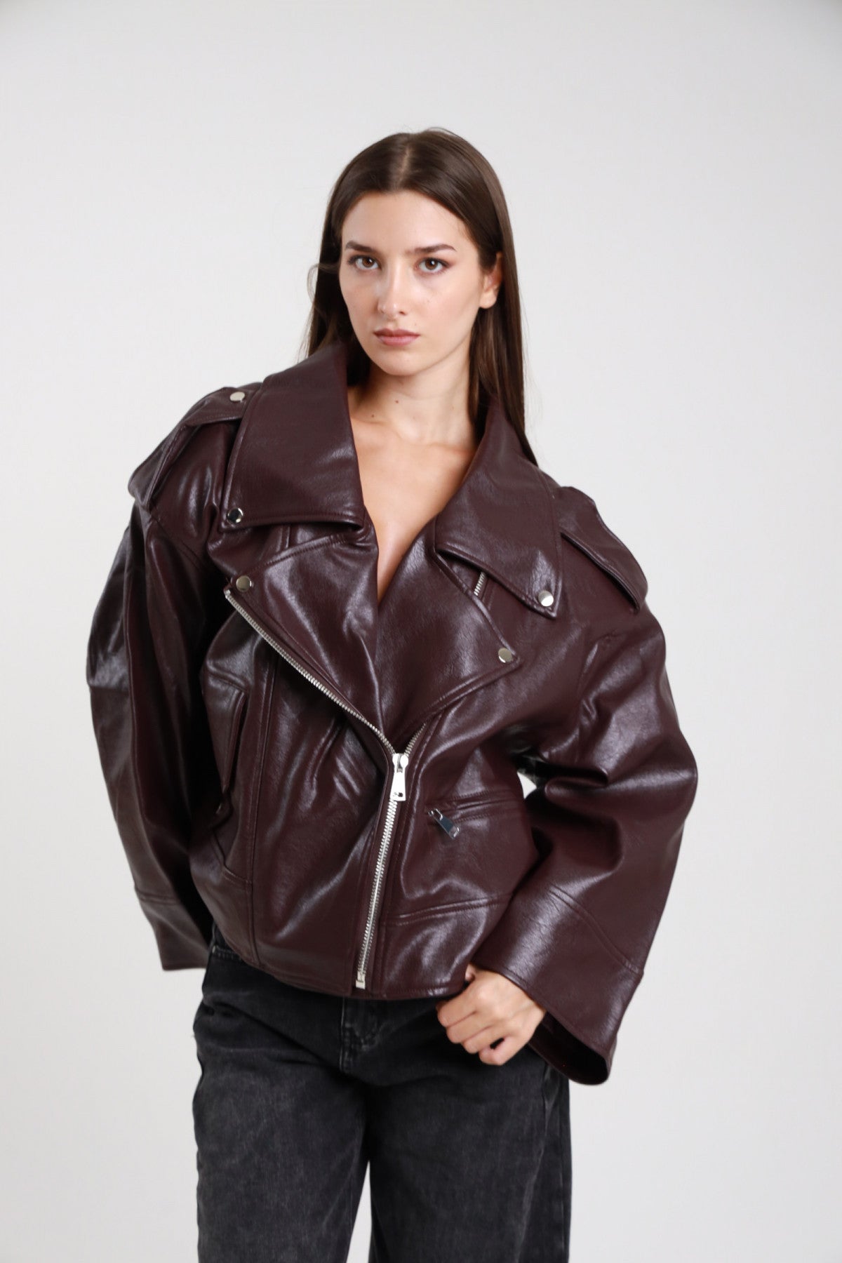 Chiodo over ecopelle bordeaux vinaccia donna oversize colletto revers ampio zip frontale asimmetrica argento tasche laterali zip - vista frontale intera mani sui fianchi con jeans neri