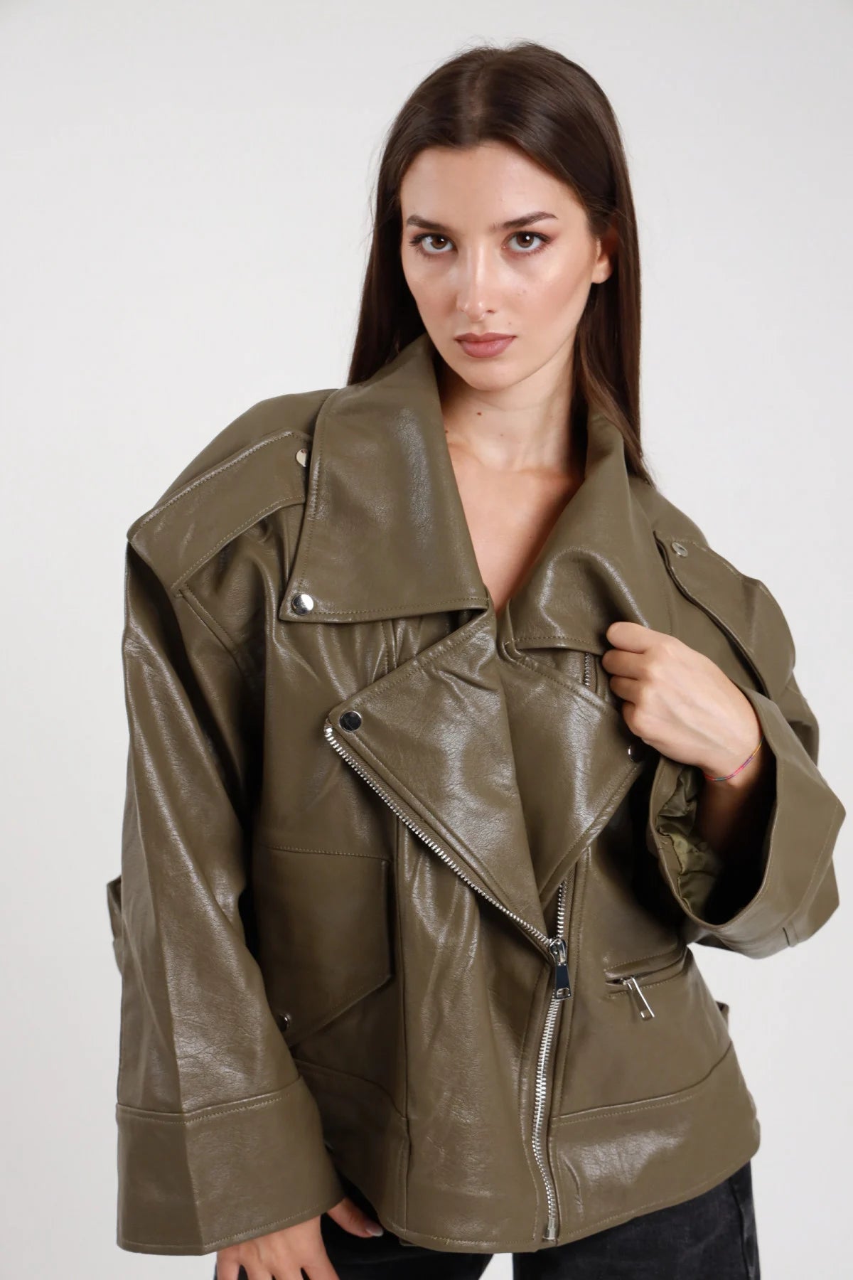 Chiodo over ecopelle verde militare kaki donna oversize colletto revers ampio zip frontale asimmetrica argento tasche zip - vista frontale tre quarti mano al colletto con jeans neri