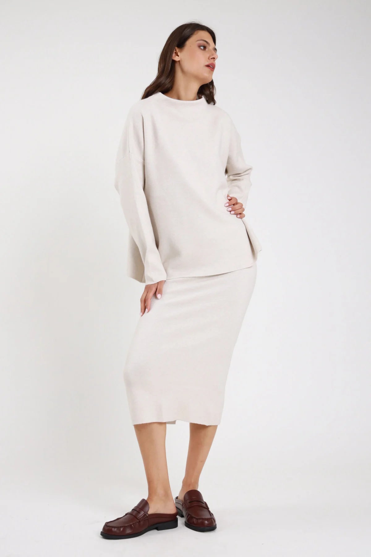 Completo coordinato gonna midi pencil coste rib maglia oversize batwing mock neck marrone cioccolato fondente frontale intera braccio alzato stivali alti marroni - modella frontale intera braccio alzato sguardo frontale capelli castani lisci raccolti sfondo bianco stivali alti marroni