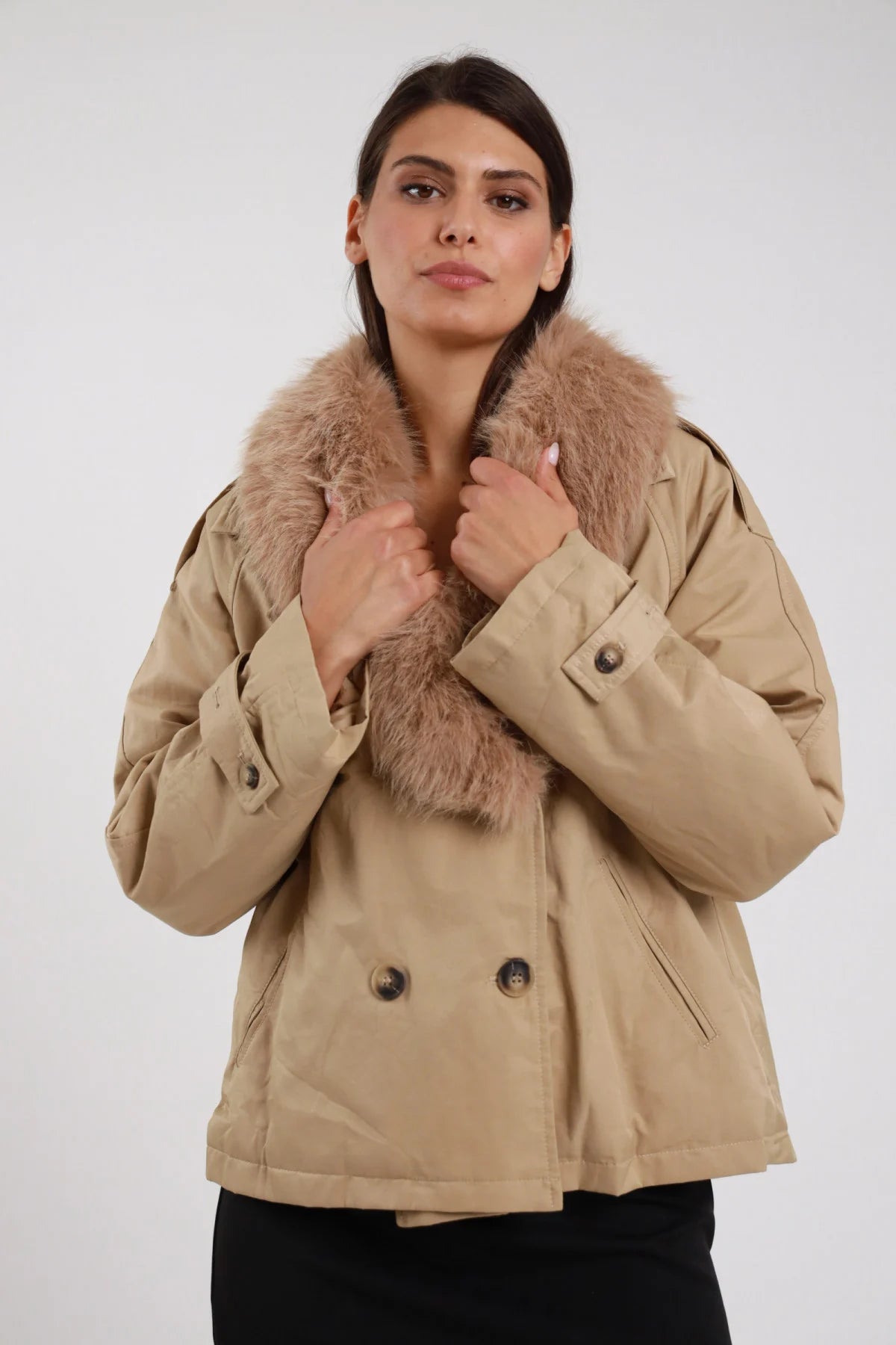 Giacca Ecopelliccia beige sabbia doppiopetto colletto sciallato ecopelliccia beige naturale rimovibile bottoni metallo brunito polsino busto frontale 3/4 mani colletto - modella busto frontale 3/4 mani colletto sguardo frontale capelli castani raccolti sfondo bianco pantalone nero