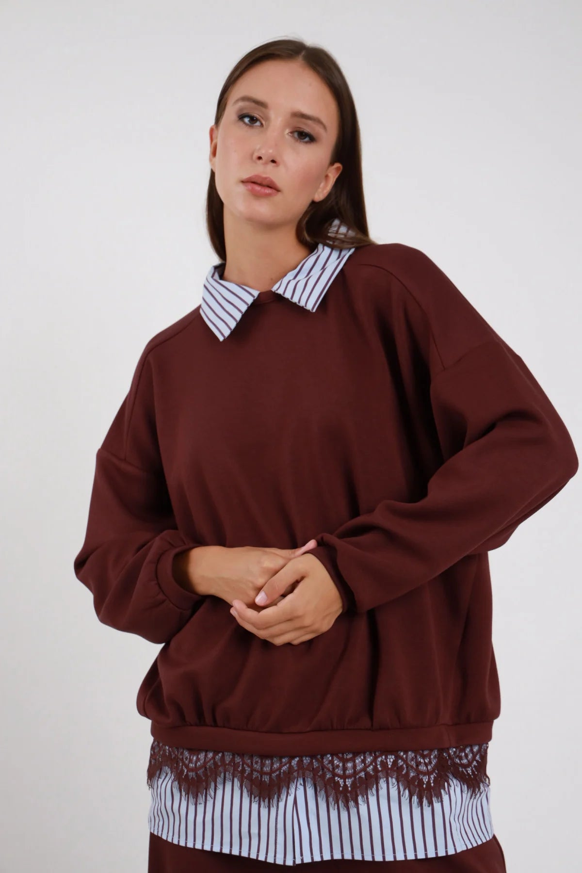 Felpa Girocollo Oversize Camicia Righe Pizzo bordeaux prugna 48% rayon colletto camicia righe bianco blu girocollo orlo camicia pizzo smerlato bordeaux nero floreale elastico fondo manica raglan ampia silhouette boxy - modella busto frontale mani intrecciate sguardo frontale soft capelli castani lisci sfondo bianco pantaloni bordeaux coordinati