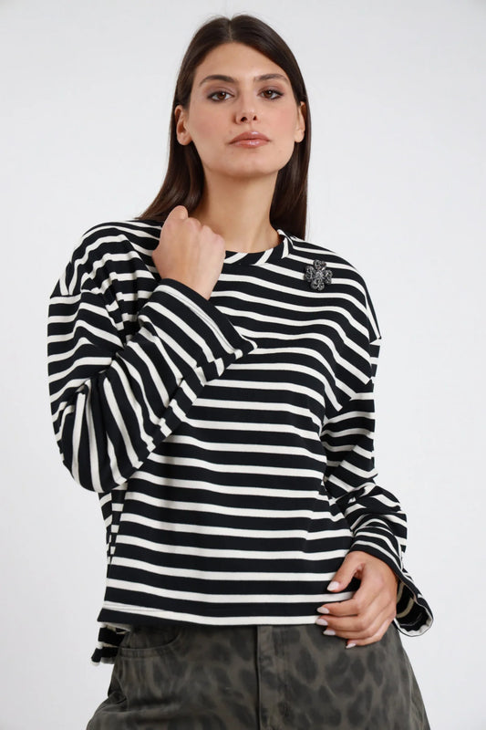 Maglia Manica Lunga Righe Marinière nero bianco panna 50% cotone collo coreana rialzato spilla gioiello floreale strass collo sx manica ampia balloon spacco polsino oversize boxy crop frontale - modella busto frontale mano collo sguardo frontale intenso capelli castani scuri sfondo bianco bermuda mimetico verde kaki