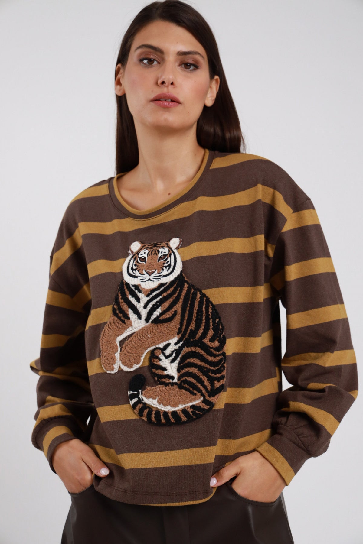 Felpa Girocollo Righe Larghe Patch Tigre marrone cioccolato ocra senape 77% cotone maxi patch tigre ricamata realistica multicolor marrone arancio bianco nero centro petto manica ampia polsino elastico oversize boxy frontale - modella busto frontale mani tasche sguardo frontale intenso capelli castani lisci sfondo bianco pantaloni ecopelle marrone scuro