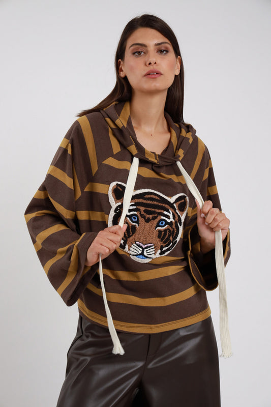Hoodie Righe Larghe Patch Testa Tigre marrone cioccolato ocra senape 77% cotone cappuccio morbido cordini panna lunghi frange maxi patch testa tigre ricamata multicolor marrone arancio nero occhi blu petto manica batwing silhouette maxi boxy crop - modella busto frontale mani tirano cordini sguardo frontale intenso capelli castani lisci sfondo bianco pantaloni ecopelle marrone