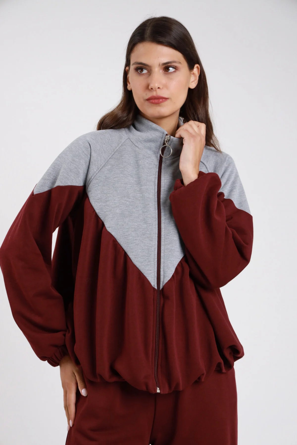 Felpa bicolor chevron diagonale grigio melange bordeaux vinaccia French Terry zip frontale anello mock-neck manica balloon oversize crop frontale tre quarti - modella frontale tre quarti mano zip sguardo laterale alto capelli castani lisci sfondo bianco pantalone felpa bordeaux coordinato