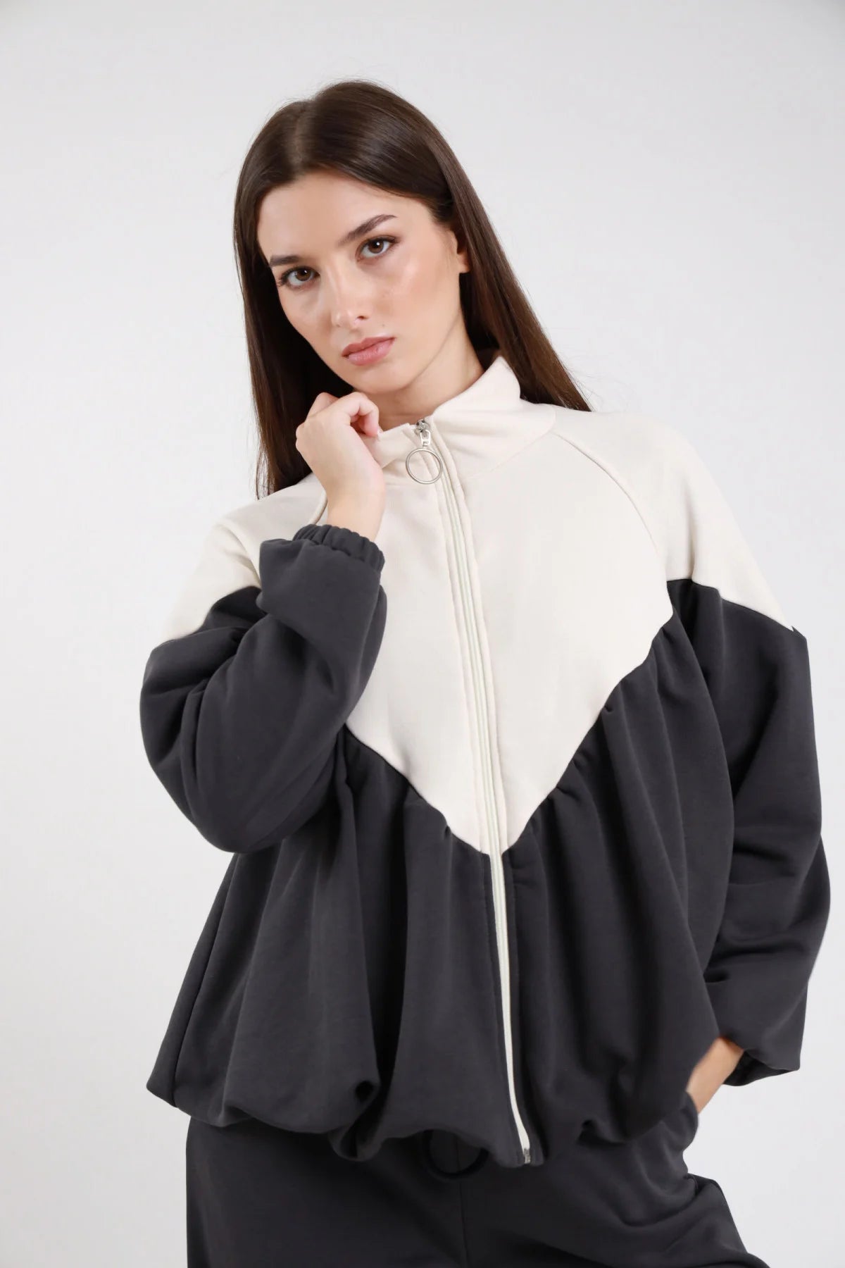 Felpa bicolor chevron diagonale bianco panna antracite French Terry zip frontale anello argento mock-neck manica balloon oversize crop frontale tre quarti chiusa - modella frontale tre quarti mano zip sguardo laterale capelli castani lisci sfondo bianco pantalone felpa nero coordinato
