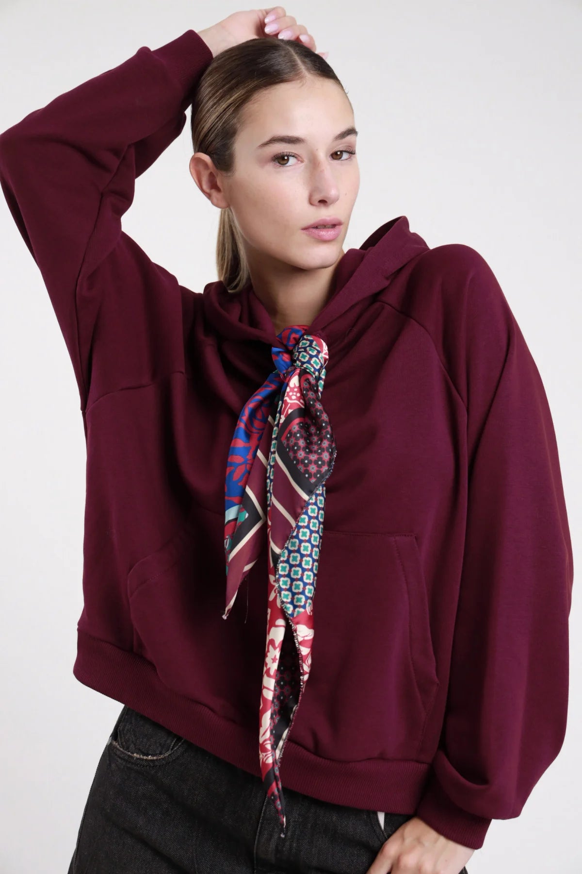 Felpa cappuccio borgogna vinaccia frontale busto mano testa foulard satin patchwork floreale geometrico annodato collo tasca kangaroo - modella frontale busto mano testa sguardo frontale jeans nero capelli castani raccolti