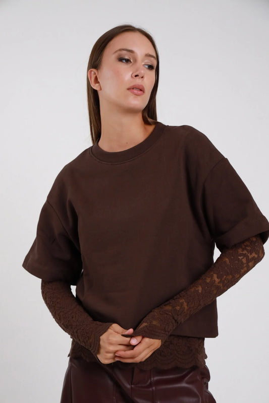 Felpa Girocollo Oversize Inserto Pizzo Floreale marrone cioccolato 100% cotone girocollo costina manica 3/4 inserto pizzo marrone tono su tono polso avambraccio silhouette boxy crop - modella busto frontale mani intrecciate sguardo frontale capelli castani lisci sfondo bianco pantaloni ecopelle marrone coordinati