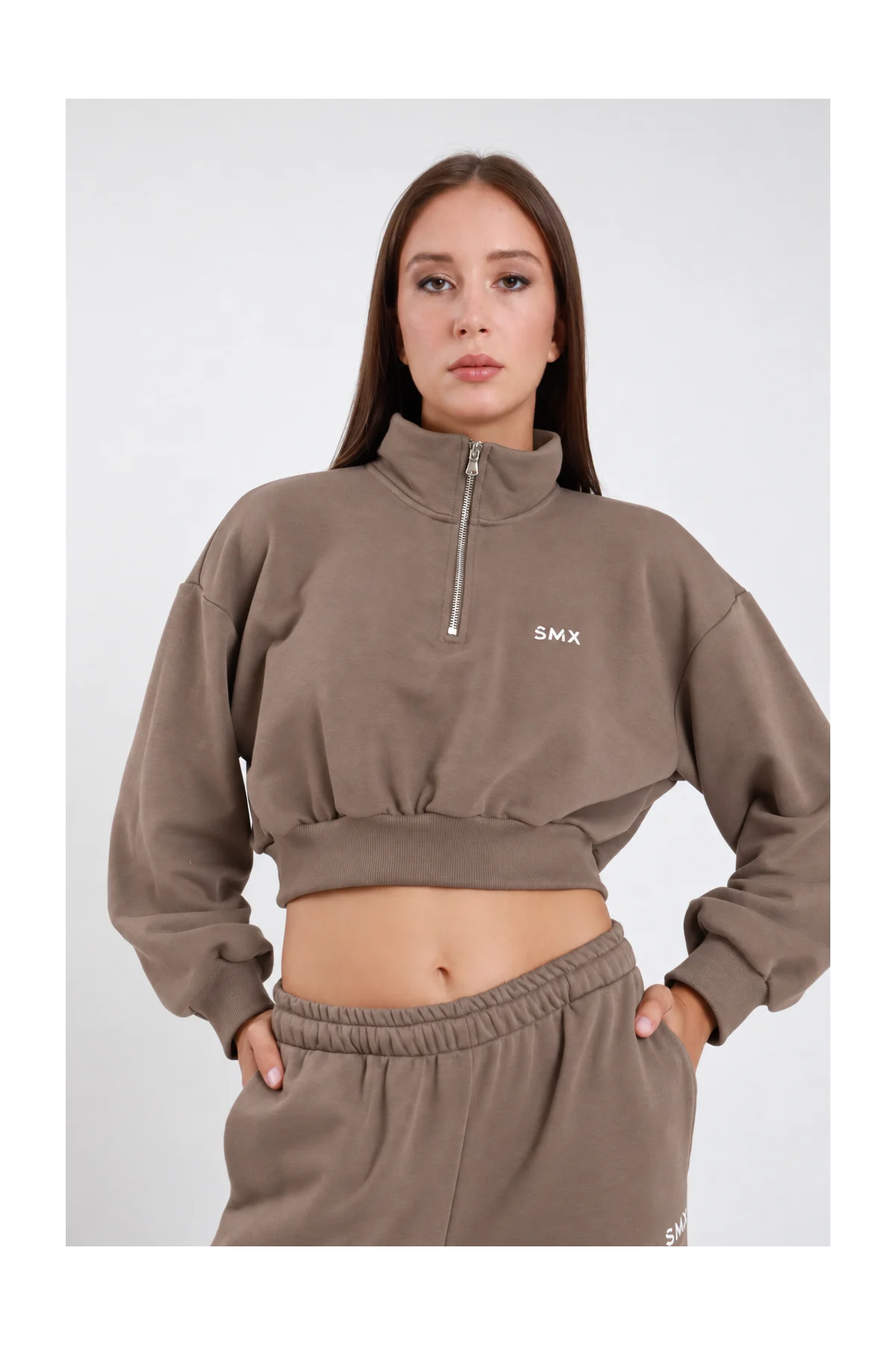 Felpa Crop Half-Zip DAYTHRU grigio taupe tortora colletto alto lupetto zip 1/2 logo SMX ricamato bianco petto manica oversize balloon orlo elastico arricciato crop busto frontale 3/4 mani tasche sguardo frontale - modella busto frontale 3/4 mani tasche sguardo frontale capelli castani lisci sfondo bianco pantalone tuta jogger taupe coordinato