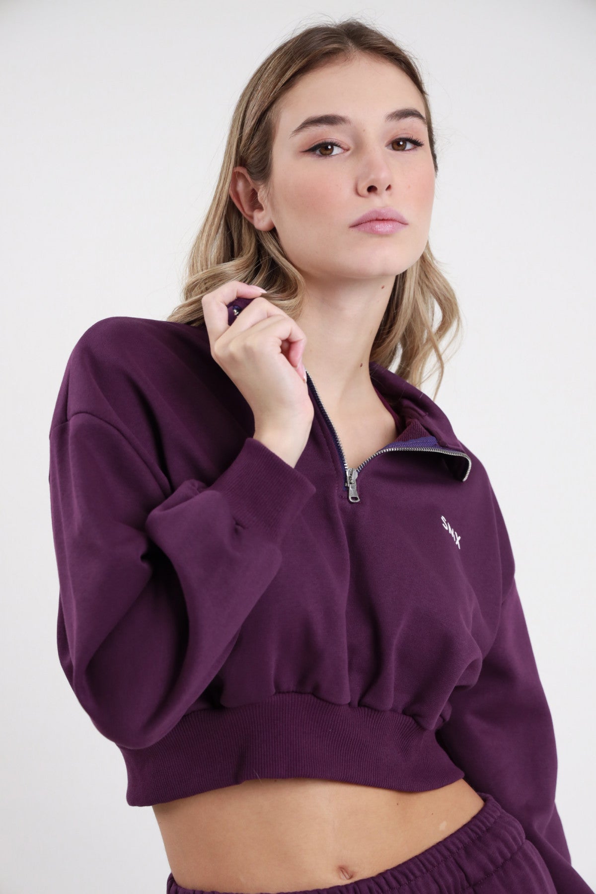Felpa Crop Half-Zip SMX Limited Edition viola melanzana colletto ribaltato polo zip 1/2 cursore argento logo SMX petto ricamato bordo costina crop busto 3/4 mano zip sguardo frontale - modella busto 3/4 mano zip sguardo frontale capelli castani lisci sfondo bianco pantalone jogger viola SMX coordinato abbinato