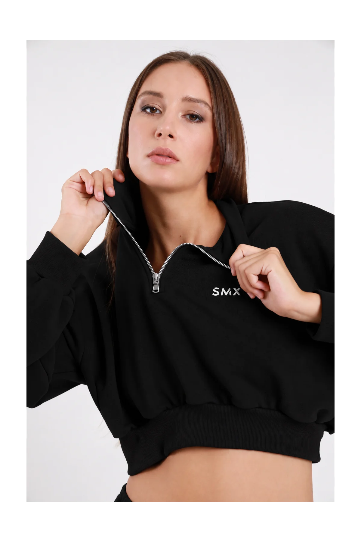 Felpa Crop Half-Zip DAYTHRU nero colletto alto lupetto zip 1/2 argento a contrasto logo SMX ricamato bianco petto manica oversize balloon orlo elastico arricciato crop busto frontale 3/4 mani colletto sguardo frontale - modella busto frontale 3/4 mani colletto sguardo frontale capelli castani lisci sfondo bianco pantalone tuta jogger nero coordinato