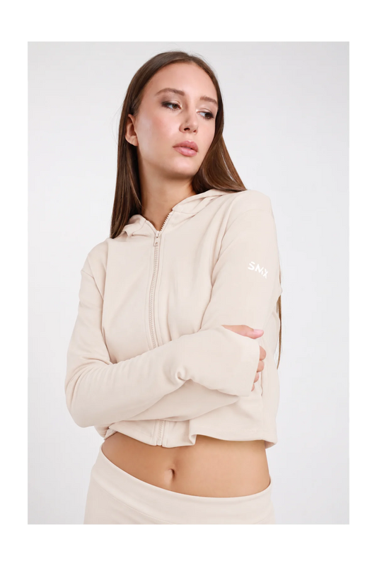 Felpa Crop Zip DAYTHRU sabbia beige chiaro cappuccio zip frontale logo SMX bianco manica sinistra orlo crop polsino foro pollice crop fit busto frontale 3/4 braccia conserte sguardo frontale - modella busto frontale 3/4 braccia conserte sguardo frontale capelli castani lisci sfondo bianco coordinato sabbia beige