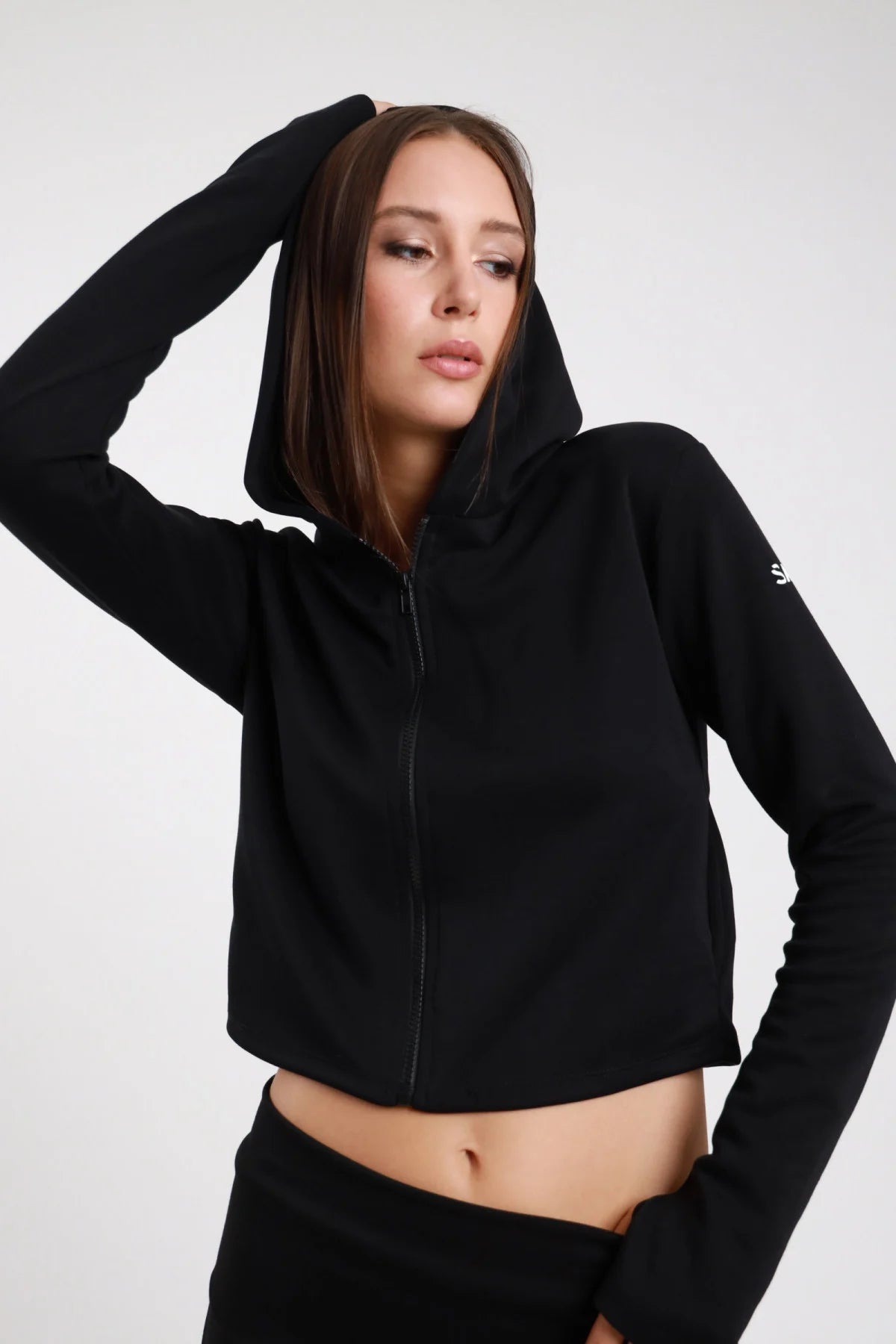 Felpa Crop Zip DAYTHRU nero cappuccio zip frontale logo SMX bianco manica sinistra a contrasto orlo crop polsino foro pollice crop fit busto frontale 3/4 mano cappuccio sguardo laterale - modella busto frontale 3/4 mano cappuccio sguardo laterale capelli castani lisci sfondo bianco coordinato nero pantalone wide-leg