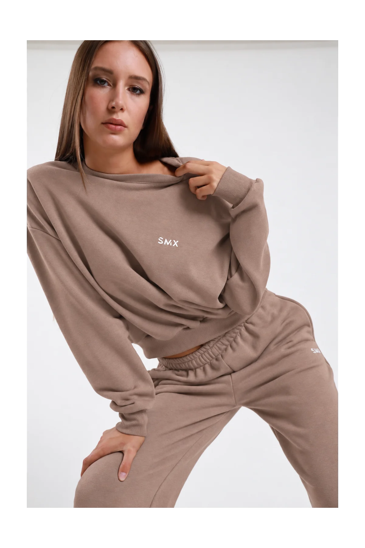 Felpa Girocollo DAYTHRU grigio taupe tortora logo SMX ricamato bianco petto sinistro girocollo costina manica oversize polsino costine boxy busto frontale 3/4 mano colletto sguardo frontale - modella busto frontale 3/4 mano colletto sguardo frontale capelli castani lisci sfondo bianco pantalone tuta jogger taupe coordinato