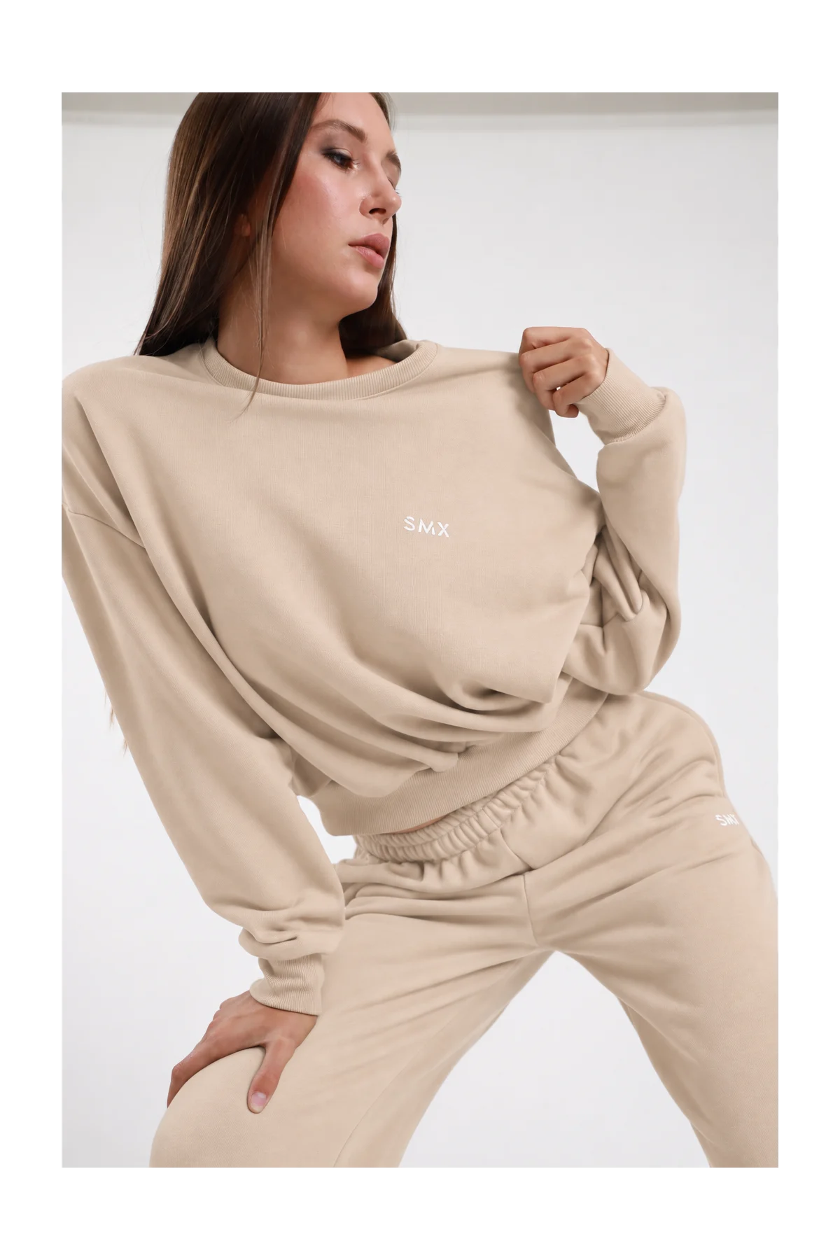 Felpa Girocollo DAYTHRU sabbia beige chiaro logo SMX ricamato bianco petto girocollo costina manica oversize polsino costine boxy busto frontale 3/4 mano colletto sguardo basso - modella busto frontale 3/4 mano colletto sguardo basso capelli castani lisci sfondo bianco pantalone tuta jogger sabbia coordinato