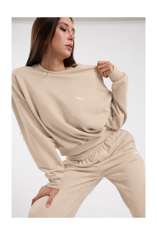 Felpa Girocollo DAYTHRU sabbia beige chiaro logo SMX ricamato bianco petto girocollo costina manica oversize polsino costine boxy busto frontale 3/4 mano colletto sguardo basso - modella busto frontale 3/4 mano colletto sguardo basso capelli castani lisci sfondo bianco pantalone tuta jogger sabbia coordinato