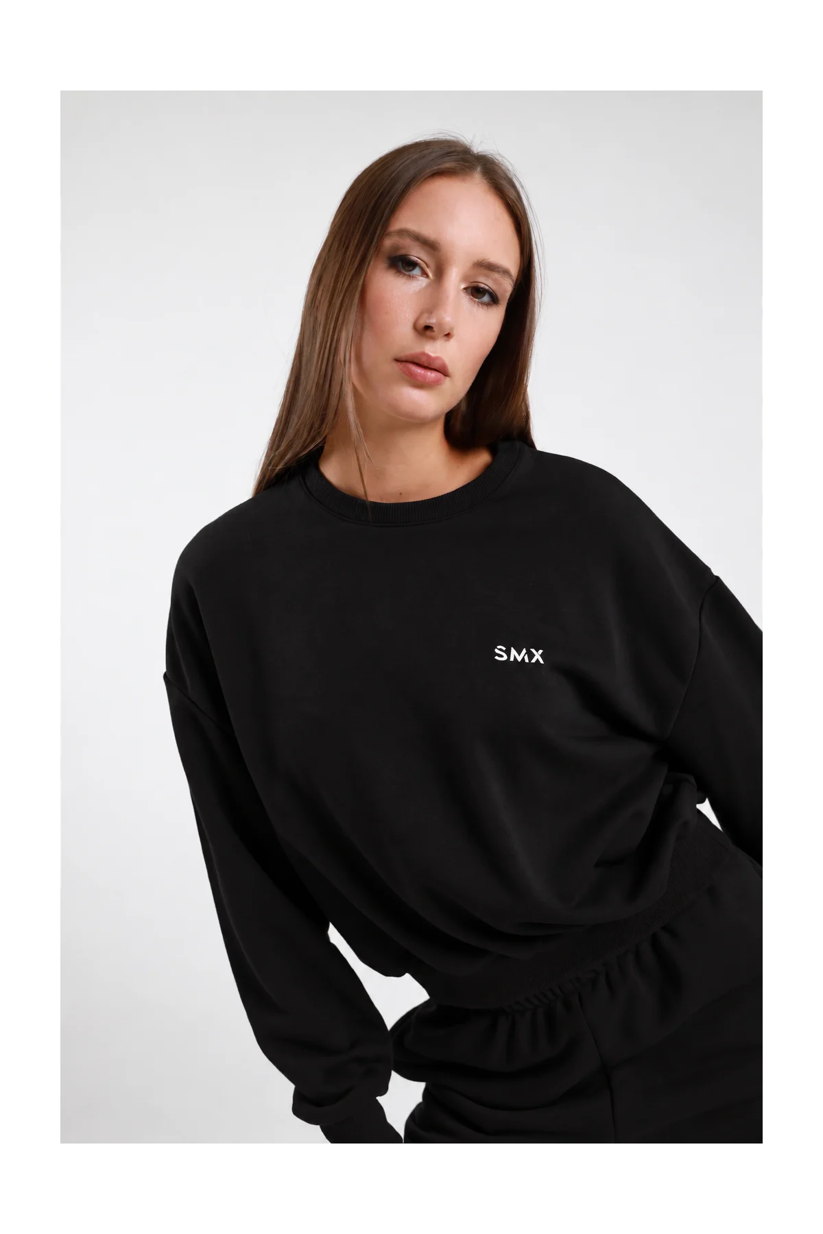 Felpa Girocollo DAYTHRU nero logo SMX ricamato bianco petto a contrasto girocollo costina manica oversize polsino costine boxy busto frontale 3/4 mano fianco sguardo frontale - modella busto frontale 3/4 mano fianco sguardo frontale capelli castani lisci sfondo bianco pantalone tuta jogger nero coordinato