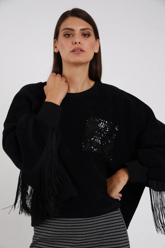Felpa Oversize Frange Tasca Paillettes nera girocollo frange lunghe nere maniche retro tasca paillettes fiore nero tono su tono silhouette boxy - modella busto frontale mano al collo sguardo intenso frontale capelli castani lisci sfondo bianco gonna midi righe grigia coordinata