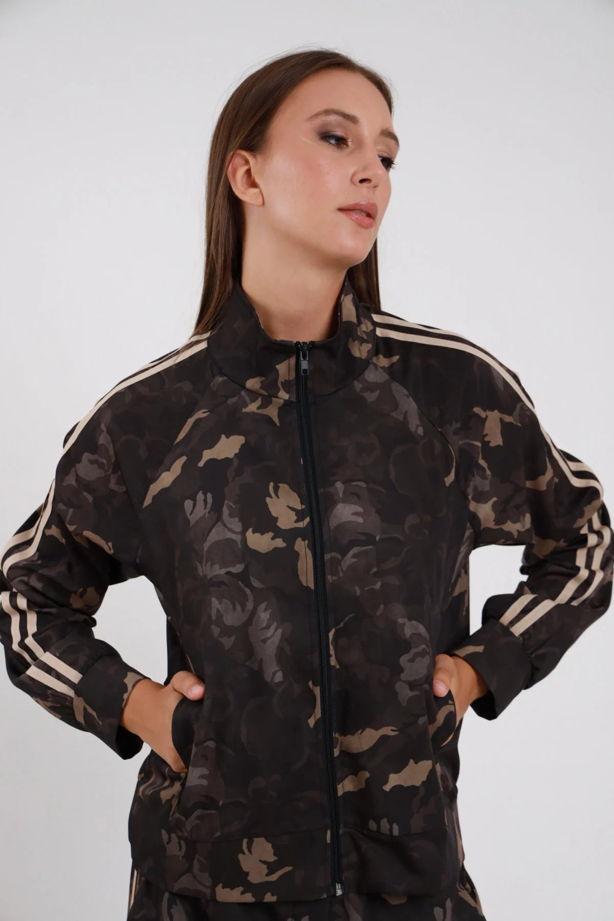 Felpa Mimetica zip full camouflage botanica khaki nero bande doppia striscia beige maniche colletto stand-up zip chiusa tasche laterali busto frontale mani tasche - modella busto frontale mani tasche sguardo laterale capelli castani bagnati sfondo bianco pantalone mimetico coordinato