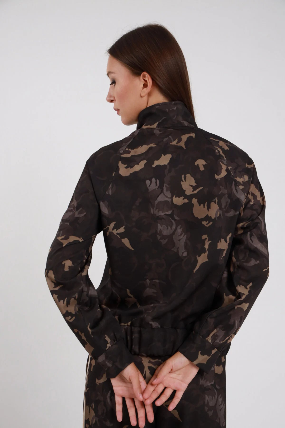 Felpa Mimetica zip full camouflage botanica khaki nero bande doppia striscia beige maniche retro colletto stand-up retro busto mani dietro schiena - modella retro busto mani intrecciate dietro schiena sguardo laterale capelli castani bagnati sfondo bianco pantalone mimetico coordinato