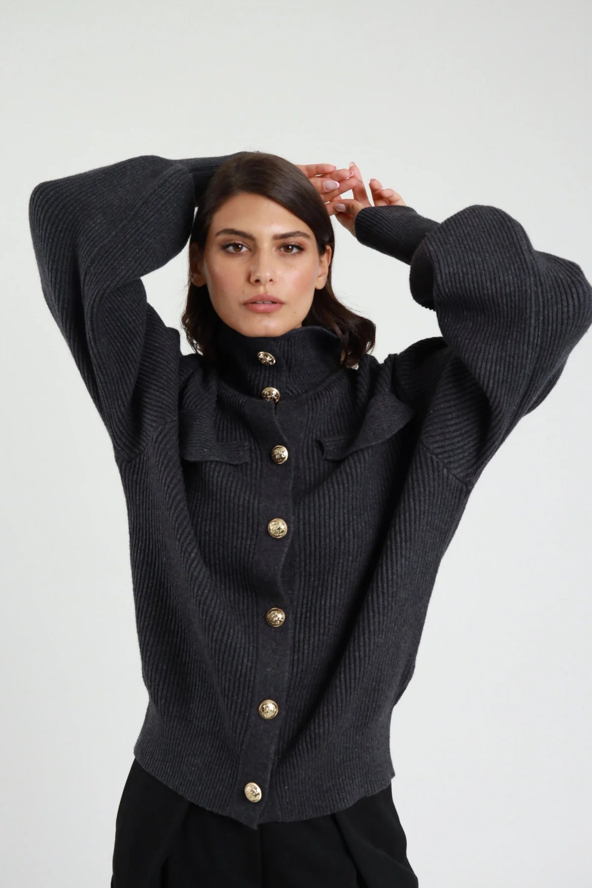Giacca in Maglia Bottone Gioiello nero coste ribbed chunky colletto alto ruffle bottoni gioiello dorati araldici manica balloon oversize crop busto frontale 3/4 mani testa colletto volant - modella busto frontale 3/4 mani testa sguardo frontale capelli castani sfondo bianco pantaloni neri
