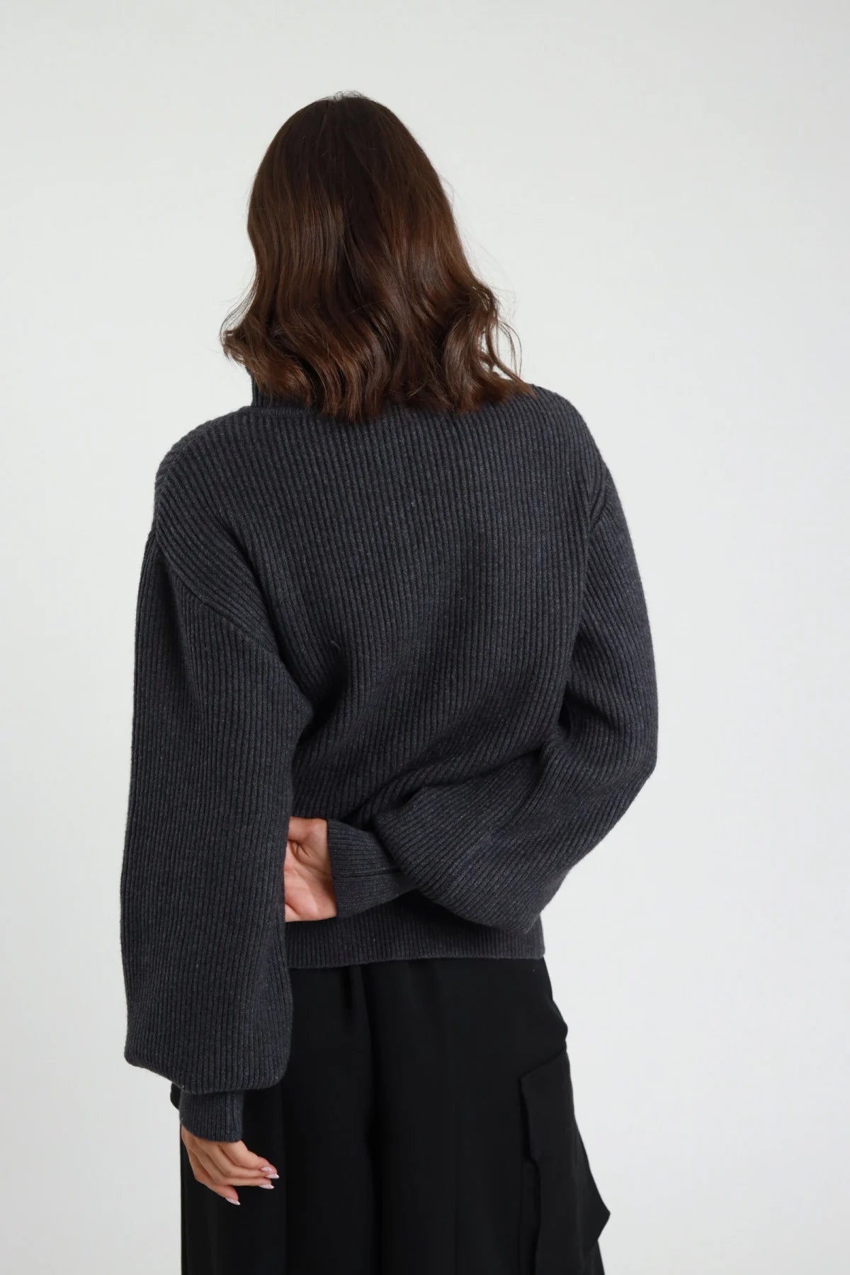Giacca in Maglia Bottone Gioiello grigio antracite coste ribbed chunky texture manica balloon oversize crop retro intera braccia aperte - modella retro intera braccia aperte sguardo laterale capelli castani sfondo bianco pantaloni neri