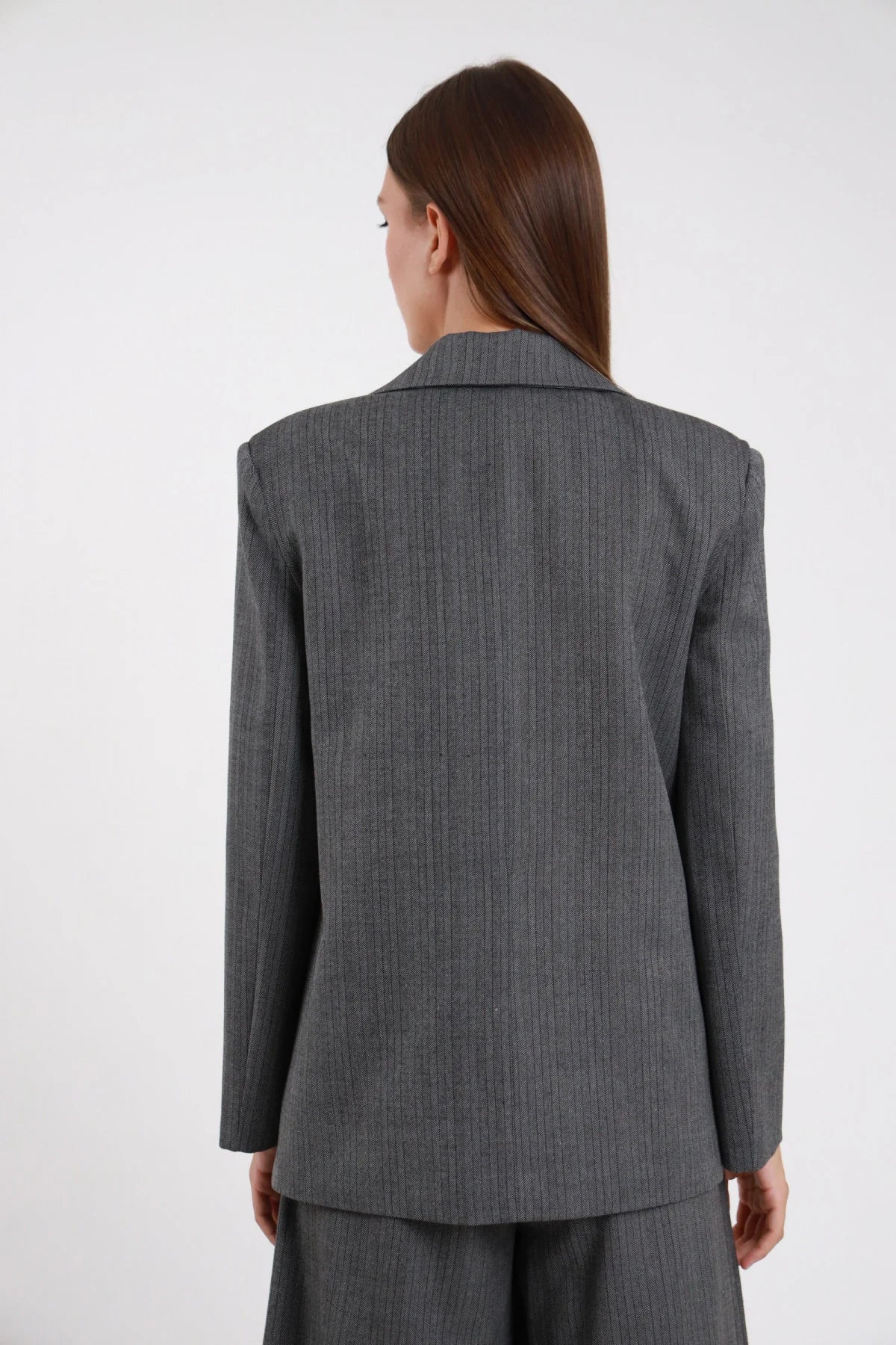 Blazer Spinato herringbone grigio antracite lurex silhouette oversize sartoriale spalle strutturate retro intera schiena - modella retro intera capelli castani lisci sfondo bianco bermuda grigio spinato