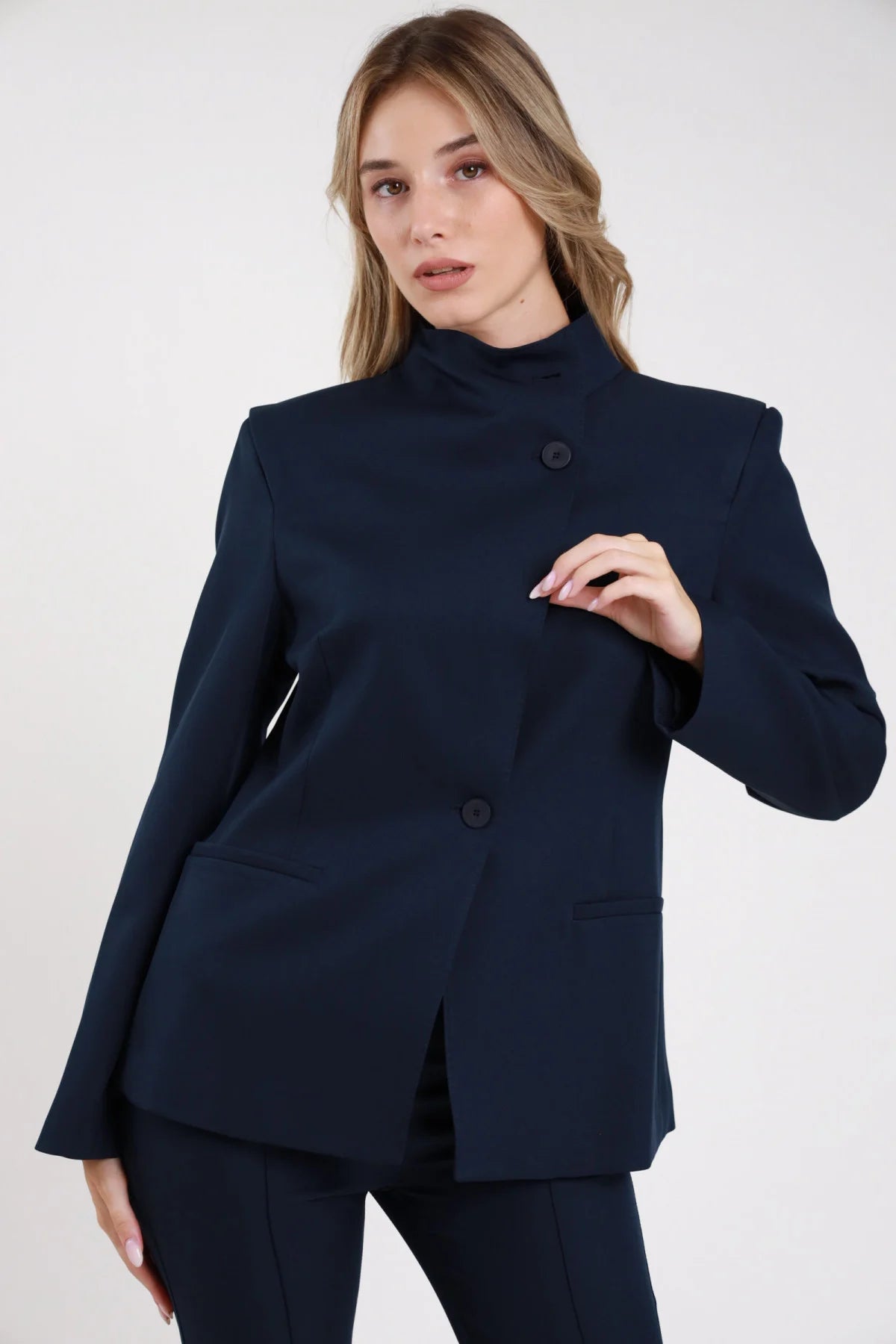 Blazer chiusura asimmetrica cioccolato marrone scuro bottone vita tasche filo - modella busto tre quarti mano in testa sguardo basso semiaperto pantalone abbinato capelli castani lisci