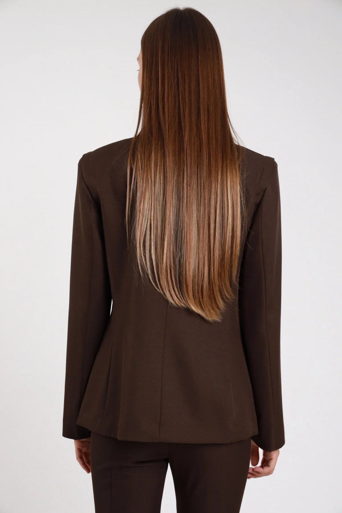 Blazer chiusura asimmetrica cioccolato marrone scuro colletto coreana frontale chiuso - modella busto frontale mani intrecciate sguardo frontale pantalone abbinato capelli castani lisci