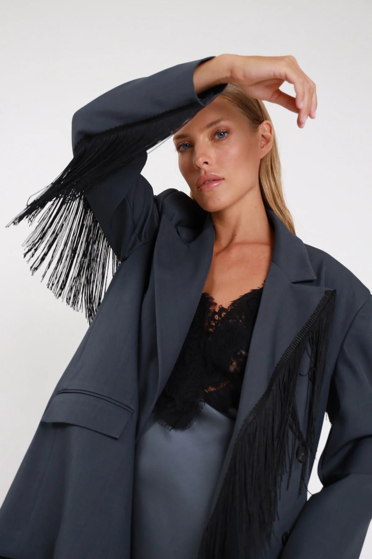 Blazer frange nere diagonali grigio antracite frontale intera doppio petto chiuso bottone centrale frange corpo - modella frontale intera sguardo frontale blazer chiuso gonna raso grigio top pizzo nero capelli biondi lisci