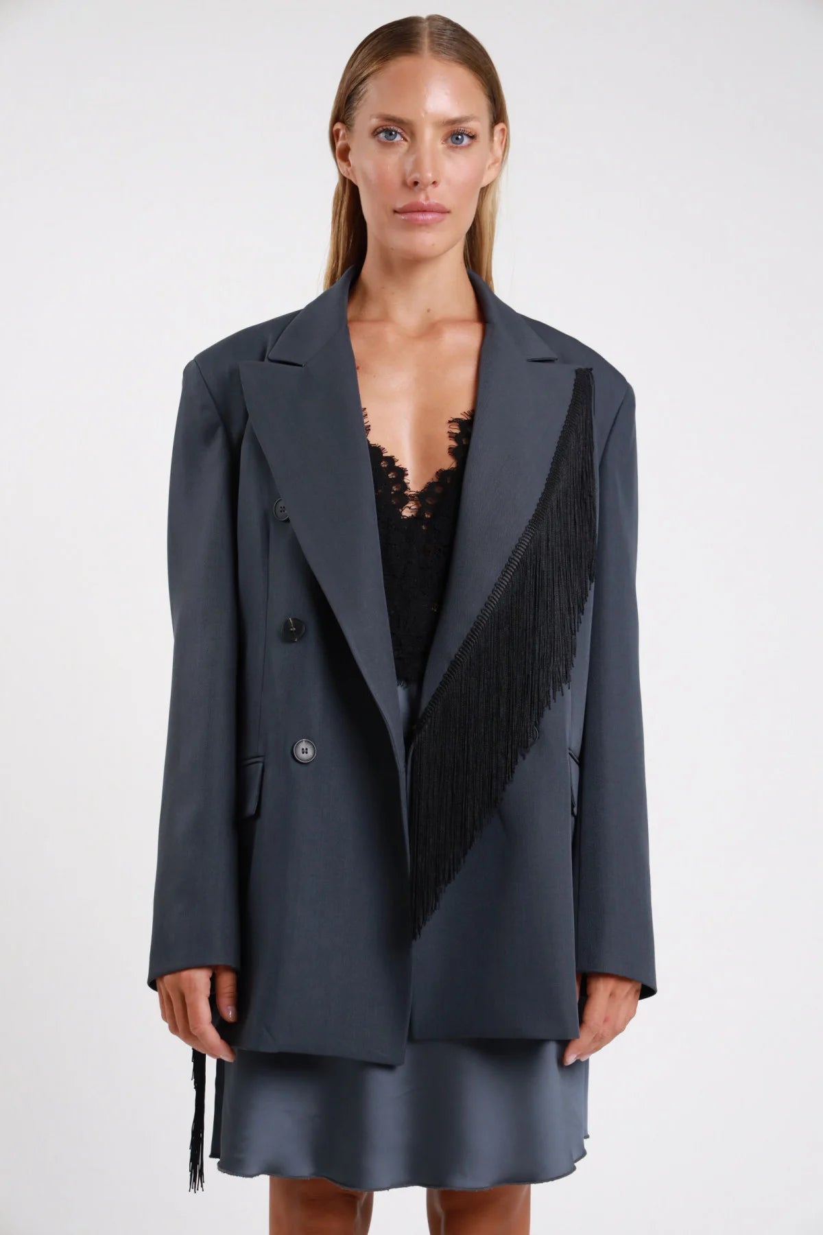 Blazer frange nere dettaglio manica polso tre quarti dinamico braccio alzato frange corpo diagonale - modella tre quarti braccio alzato sguardo frontale frange manica polso corpo grigio antracite gonna raso grigio capelli biondi