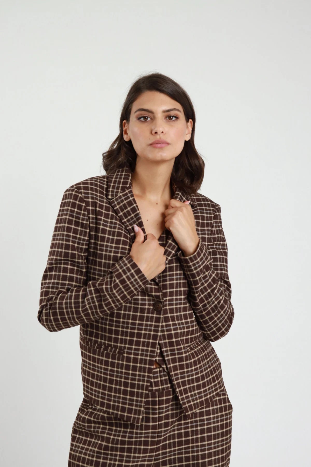 Blazer Corto Check tartan marrone cioccolato quadri panna revers V 2 bottoni tasche filetto patta spalle strutturate frontale busto mani revers - modella frontale busto mani revers sguardo frontale capelli castani scuri sfondo bianco pantalone check marrone