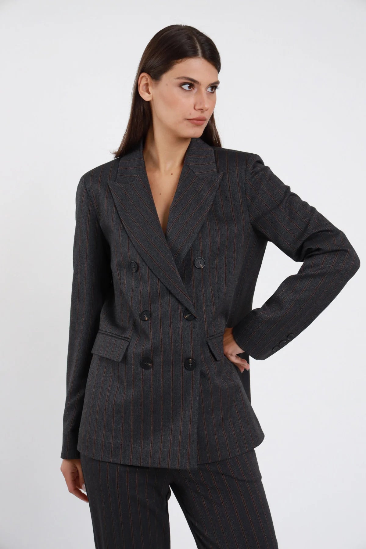 Blazer doppiopetto gessato Susy Mix Pre-Fall grigio antracite pinstripe bordeaux doppiopetto 6 bottoni 2 tasche patta spalle strutturate power shoulder revers lancia semi-fitted anca frontale intera mano fianco sguardo laterale - modella frontale intera mano fianco sguardo laterale capelli scuri lisci sfondo bianco pantalone gessato coordinato tailleur abbinato