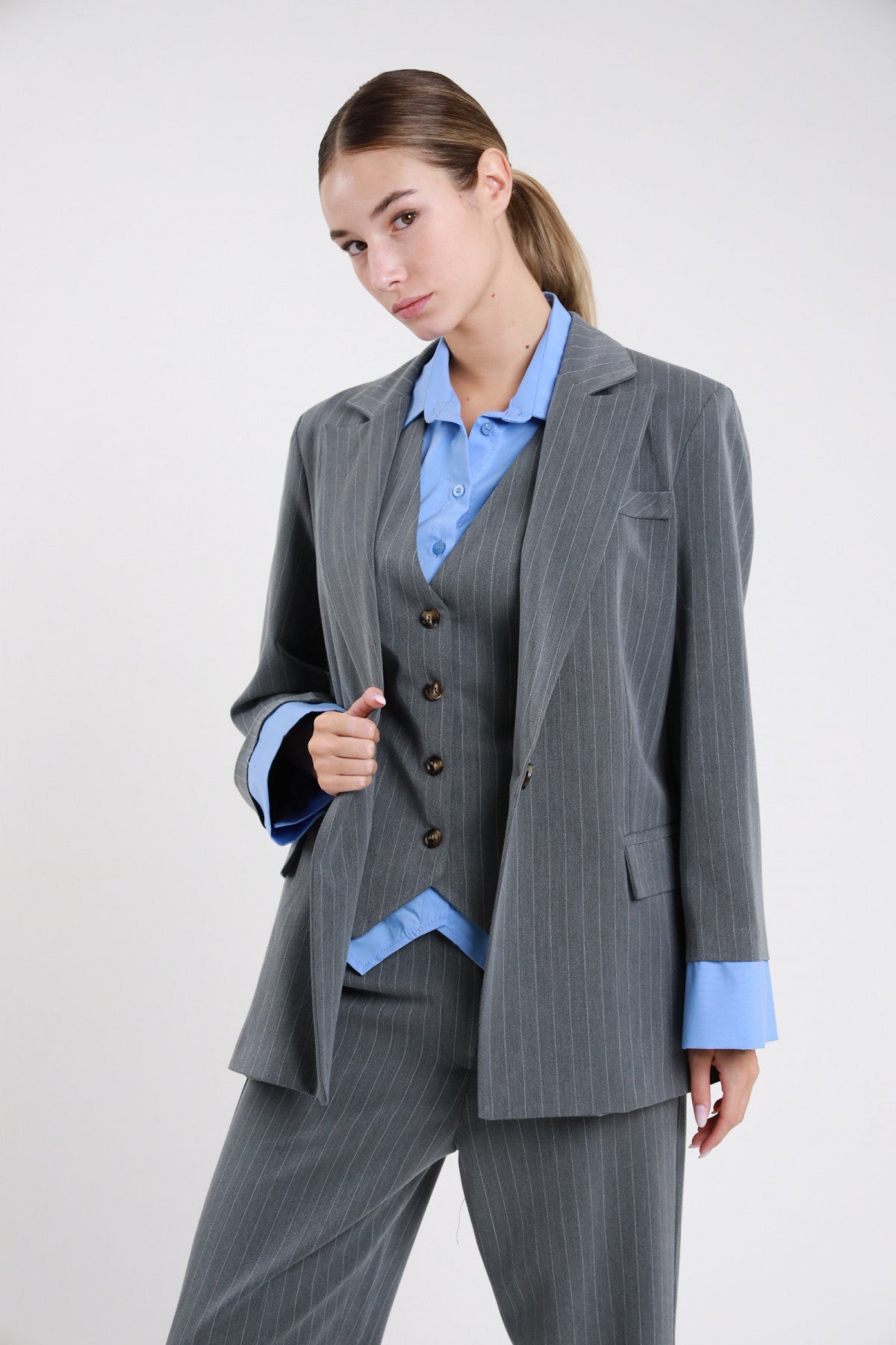 Blazer gessato grigio oversize con camicia azzurra - modella busto tre quarti con gilet gessato e pantaloni grigi coordinati