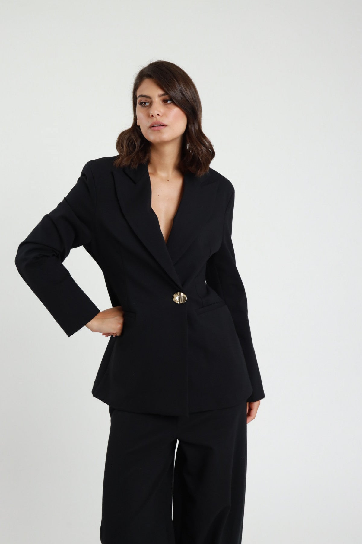 Blazer Punto Milano nero revers V profondo bottone dorato decorativo tasche filetto patta spalle strutturate frontale intera mano fianco - modella frontale intera mano fianco sguardo frontale capelli castani scuri sfondo bianco pantalone uovo nero kitten heel neri