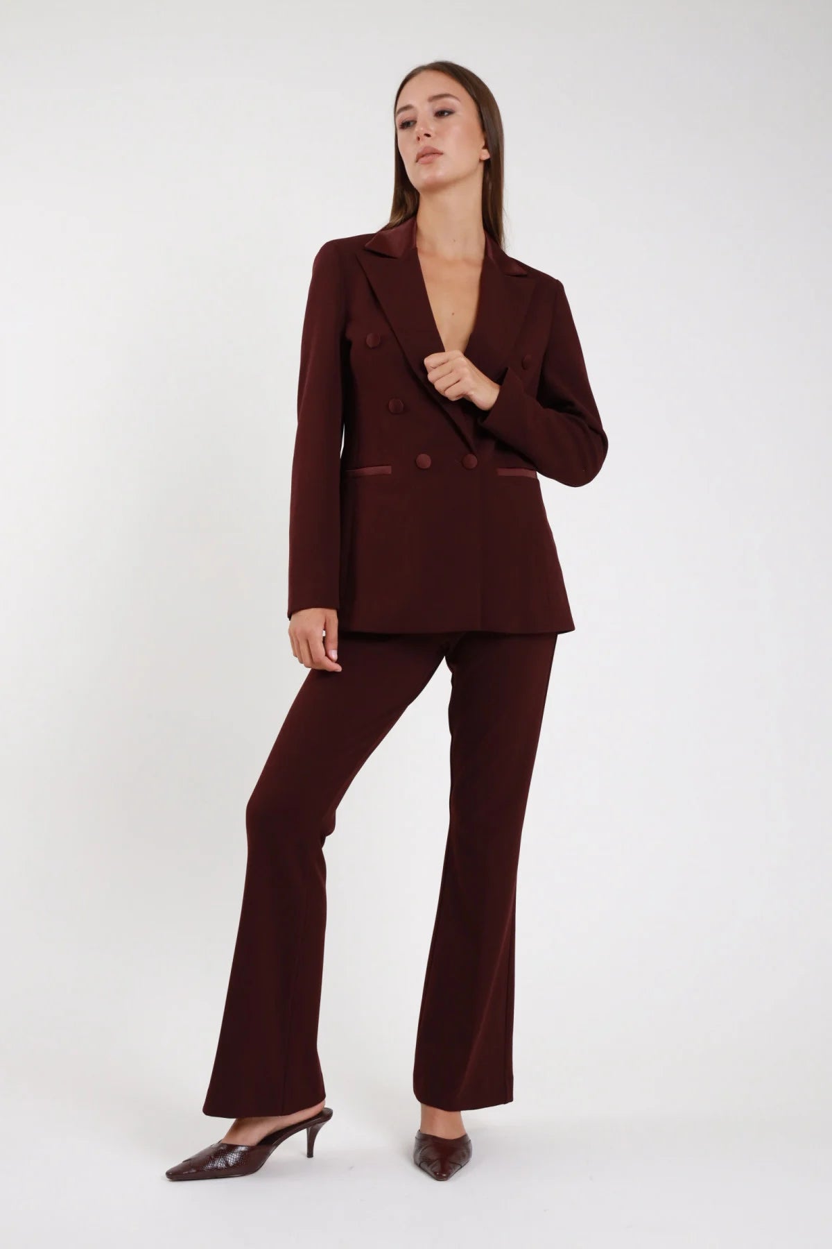 Completo tailleur blazer doppio petto bordeaux amaranto raso pantalone flare - modella frontale intera mano al blazer sguardo laterale mules marroni capelli castani lisci