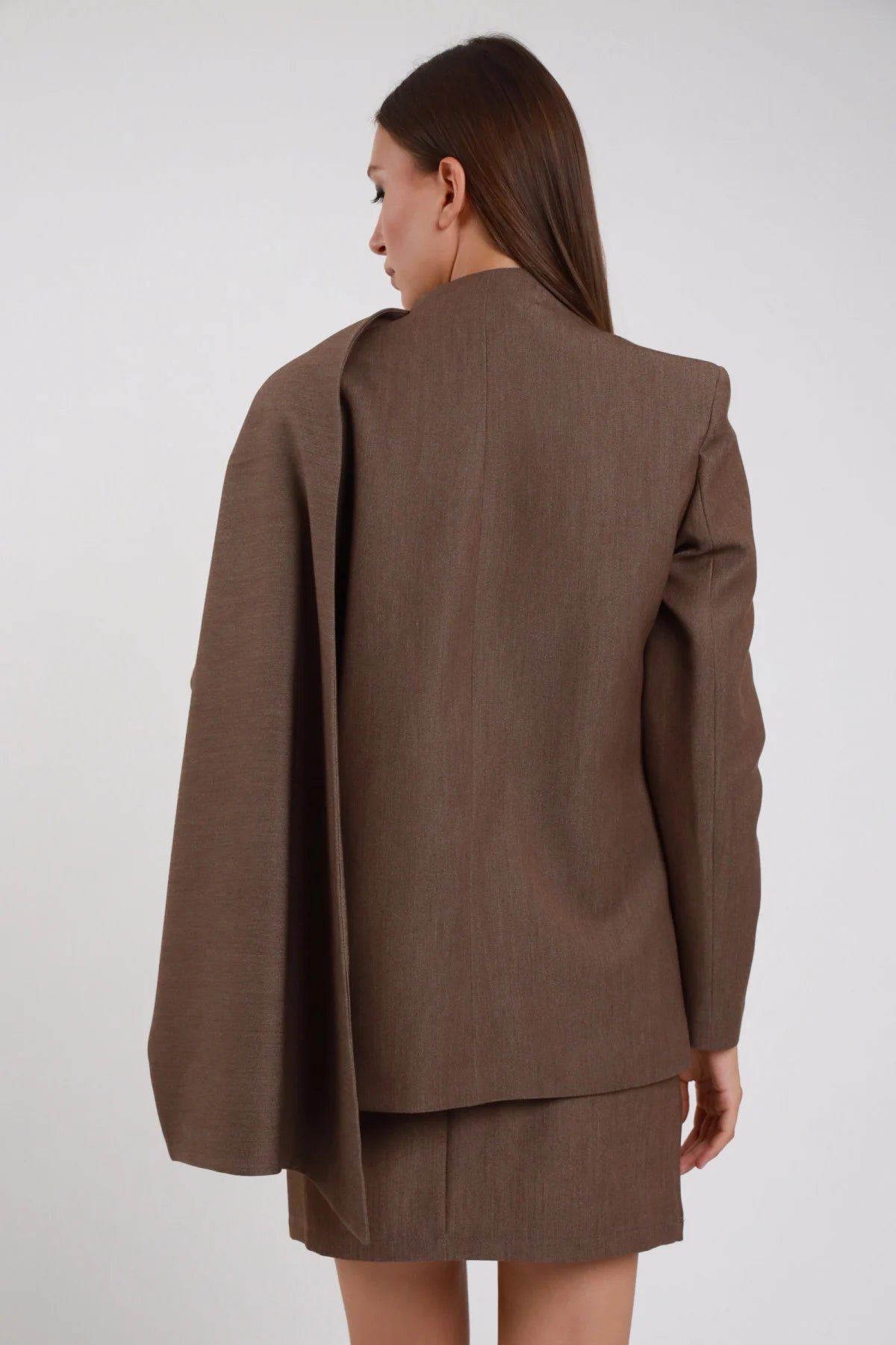 Blazer Scialle marrone cioccolato scialle mantella cascante retro silhouette spalle strutturate manica slim retro intera schiena sguardo laterale - modella retro intera sguardo laterale capelli castani lisci sfondo bianco minigonna marrone coordinata