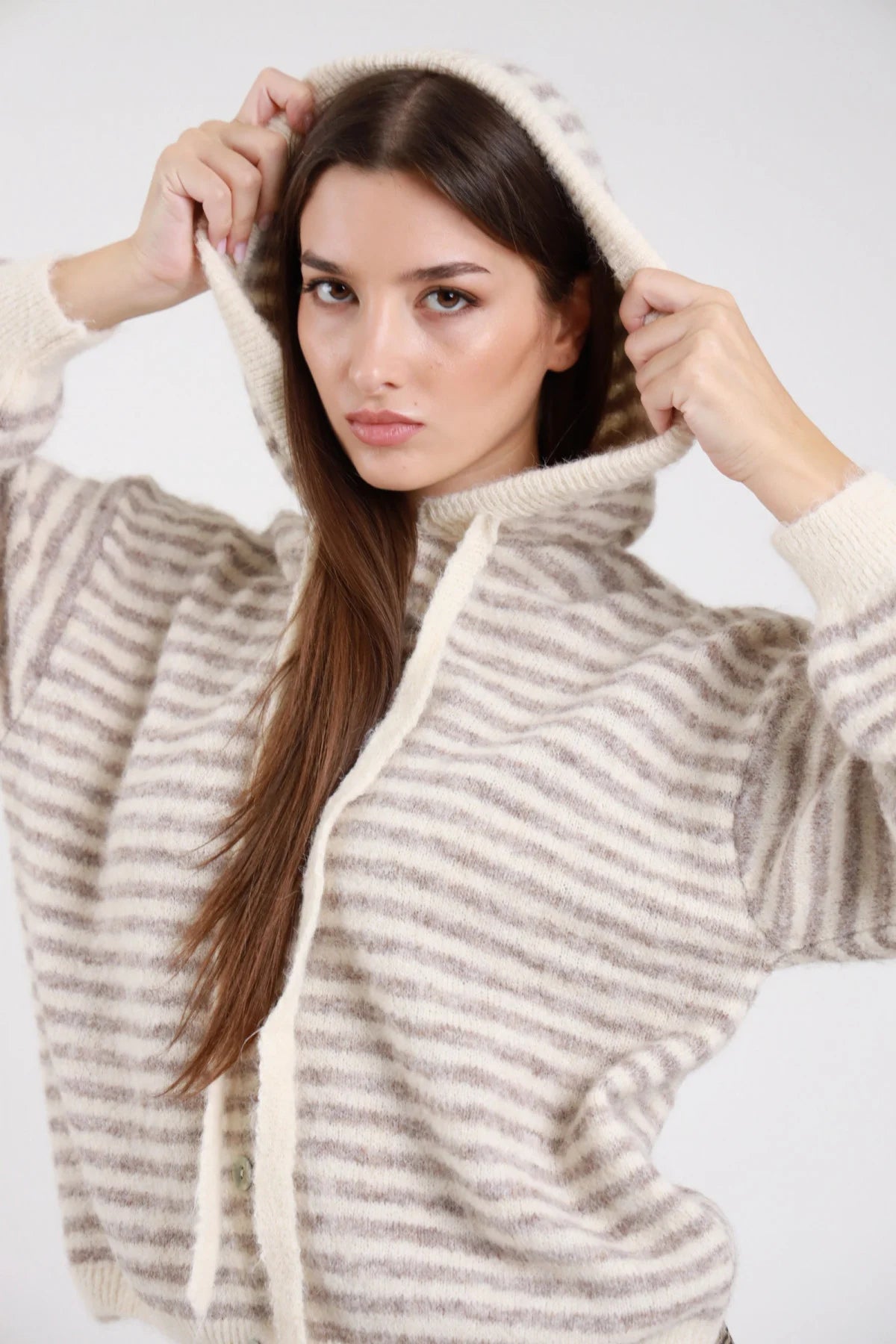 Felpa cardigan maglia bouclé eyelash righe bold bicolor avorio crema beige greige cappuccio cordoncino bottoni madreperlati batwing oversize boxy frontale busto cappuccio in testa mani cordoncino - modella frontale busto mani cappuccio cordoncino sguardo frontale capelli castani scuri lisci sfondo bianco pantaloni check beige