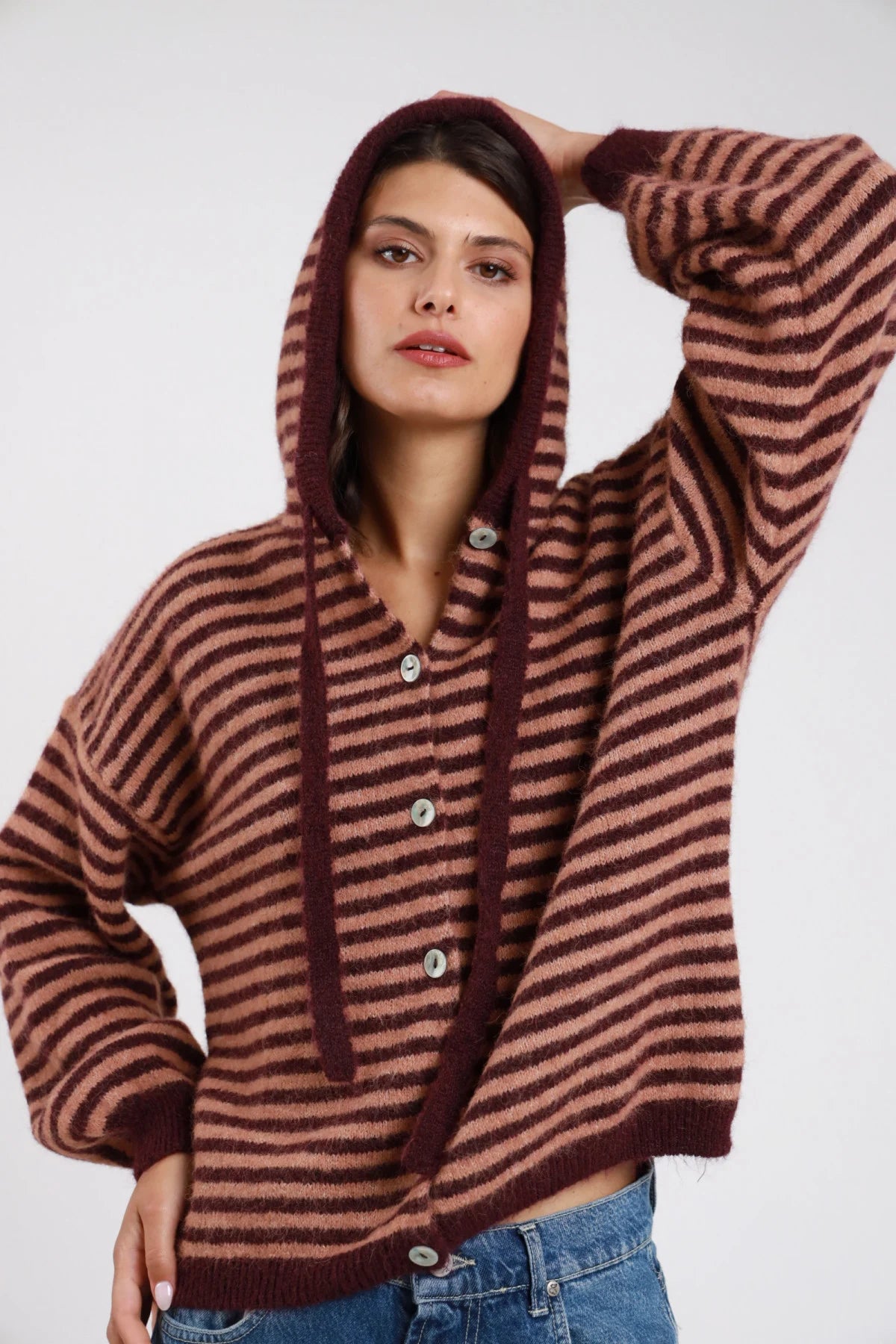Felpa cardigan maglia bouclé eyelash righe bold bicolor bordeaux vinaccia rosa cipria cappuccio cordoncino bottoni madreperlati batwing oversize boxy frontale busto cappuccio in testa braccia aperte - modella frontale busto cappuccio in testa braccia aperte sguardo frontale capelli castani scuri lisci sfondo bianco jeans blu