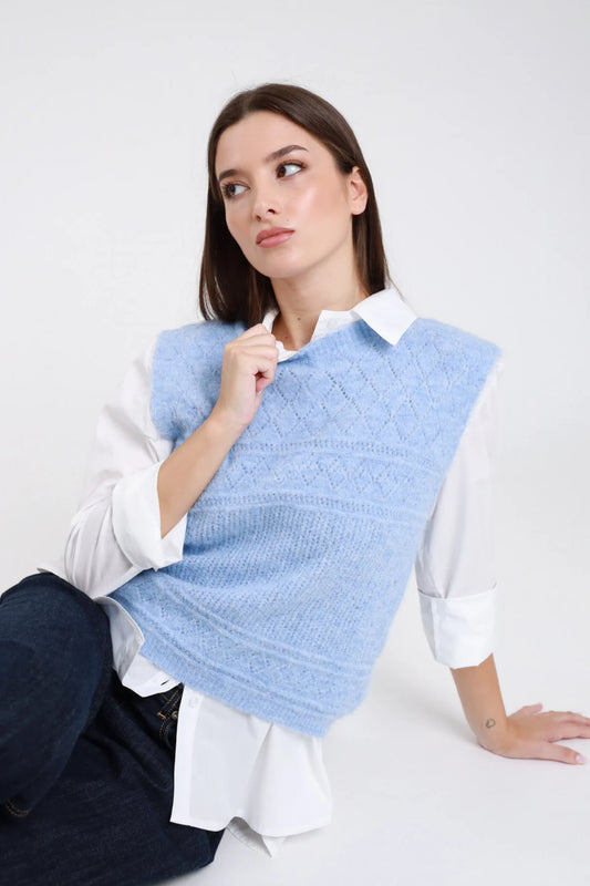 Gilet maglia eyelash bouclé traforato rombi senza maniche girocollo crop azzurro celeste baby blue frontale seduta mano scollo camicia bianca jeans blu - modella frontale seduta mano scollo sguardo laterale capelli castani scuri lisci sfondo bianco camicia bianca jeans blu scuro