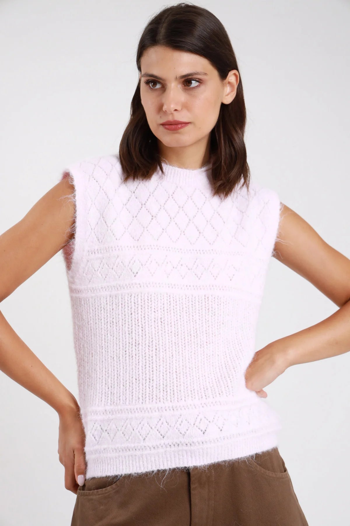 Gilet maglia eyelash bouclé traforato rombi senza maniche girocollo crop bianco latte panna frontale busto mani fianchi pantaloni marroni - modella frontale busto mani fianchi sguardo laterale capelli castani scuri ondulati sfondo bianco pantaloni marroni cargo