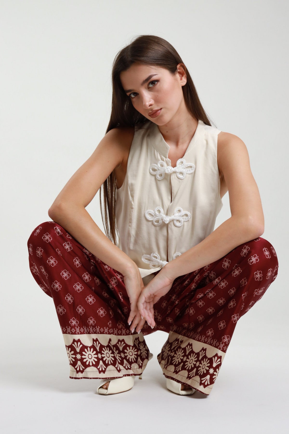 Gilet alamari panna con chiusure intrecciate abbinato a pantaloni palazzo bordeaux – vista frontale seduta