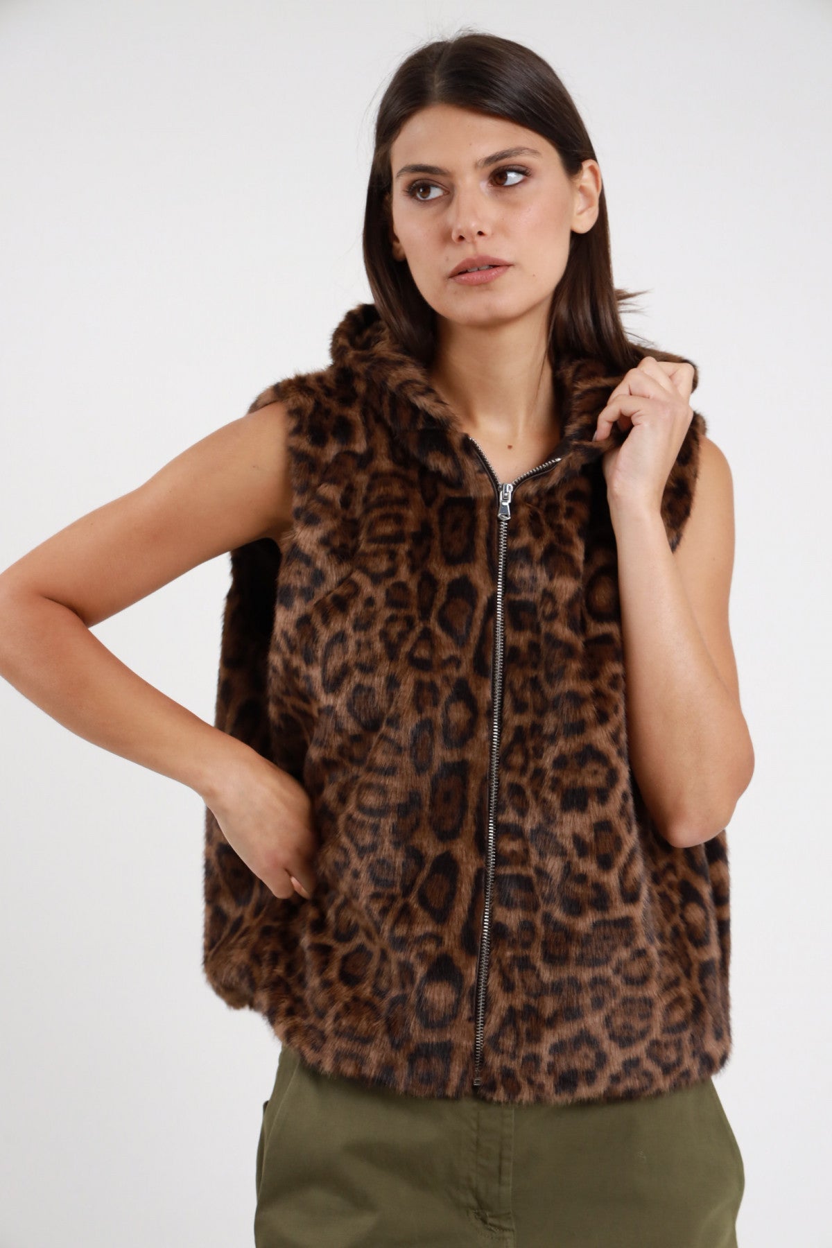 Gilet ecopelliccia animalier leopard cappuccio Susy Mix Pre-Fall stampa maculata leopard marrone tabacco zip frontale cursore argento tasche laterali nascoste pelo cappuccio abbassato spalle frontale busto mano tasca sguardo laterale - modella busto frontale mano tasca sguardo laterale capelli scuri lisci sfondo bianco pantaloni verde militare cargo abbinati