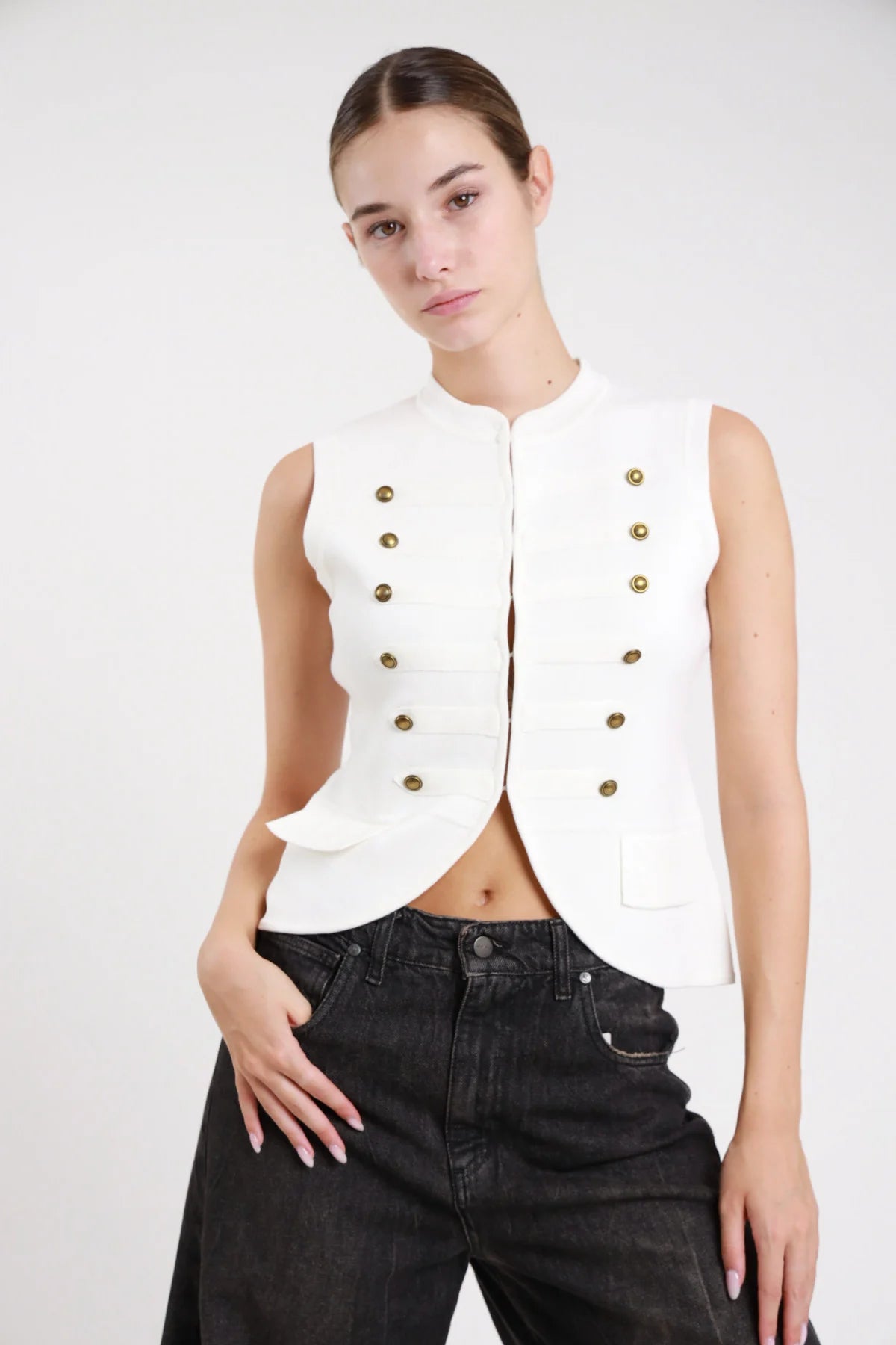 Gilet militare hussard maglia cioccolato dinamico braccia alzate dettaglio bottoni dorati passant - modella frontale braccia alzate sguardo laterale jeans blu capelli castani lisci