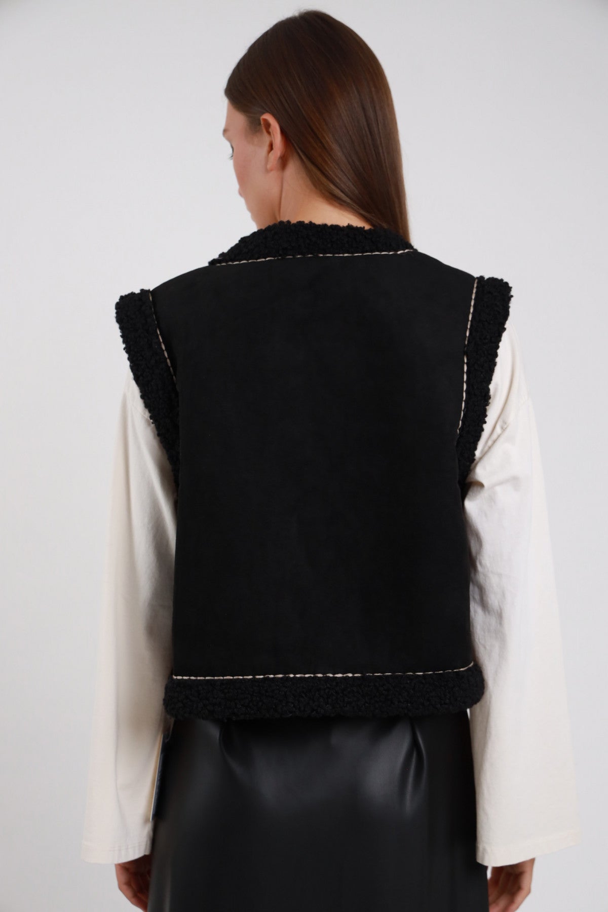 Gilet Ecomontone Ricamato nero retro liscio bordi bouclé bianchi a contrasto cuciture orizzontali decorative silhouette crop retro intera schiena - modella retro intera capelli castani lisci sfondo bianco camicia bianca gonna ecopelle nera