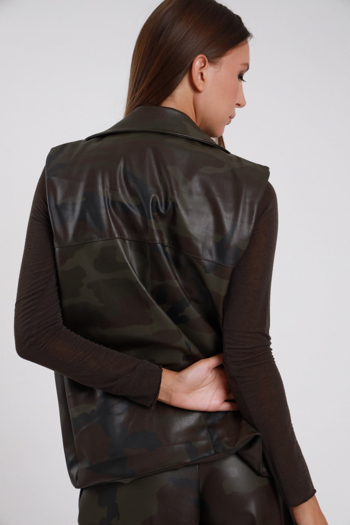 Gilet Mimetico biker ecopelle PU camouflage verde bronzo cuciture sartoriali retro senza maniche lunghezza sotto vita retro busto 3/4 - modella retro busto 3/4 sguardo abbasso capelli castani sfondo bianco bermuda mimetico coordinato top marrone