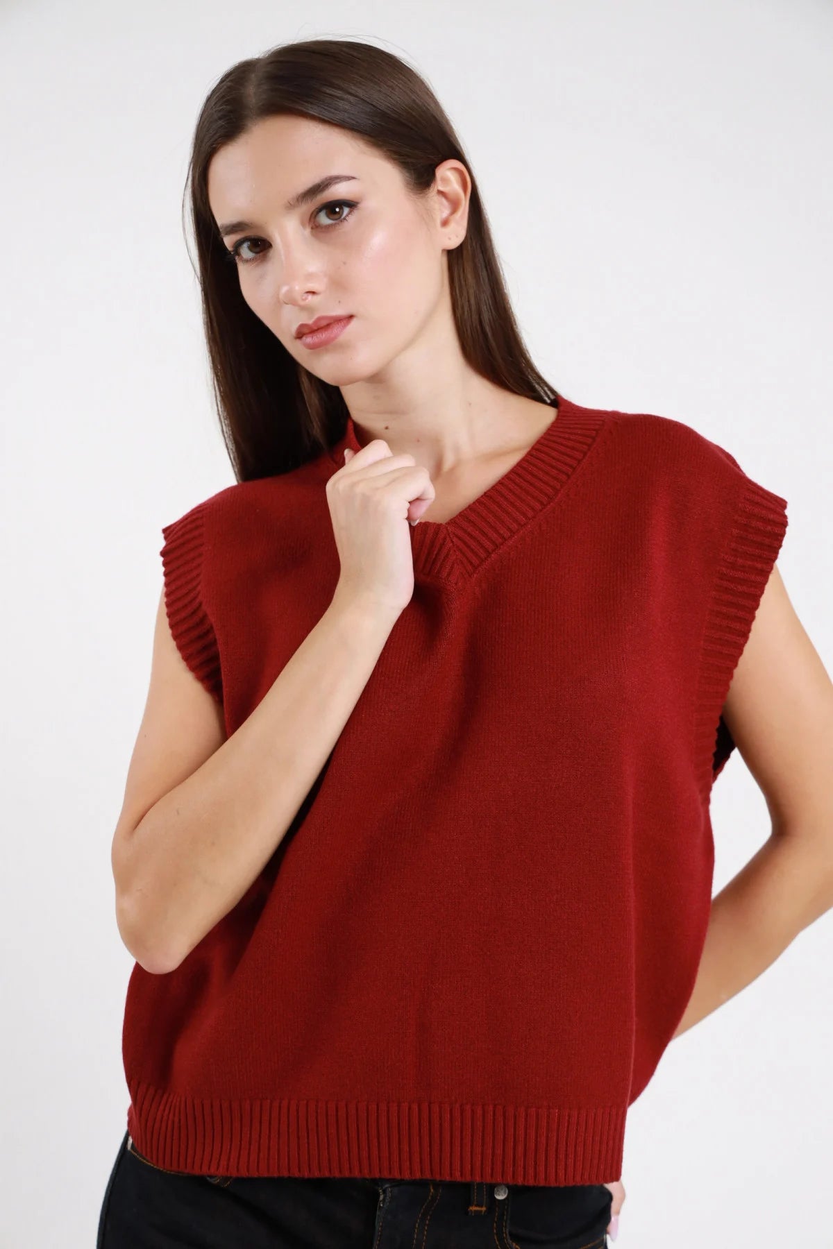 Gilet V maglia panna bianco latte donna boxy cropped scollo V bordino costine cap-sleeve spalle dropped - vista frontale mezzo busto seduta mano al collo con pantaloni ecopelle neri