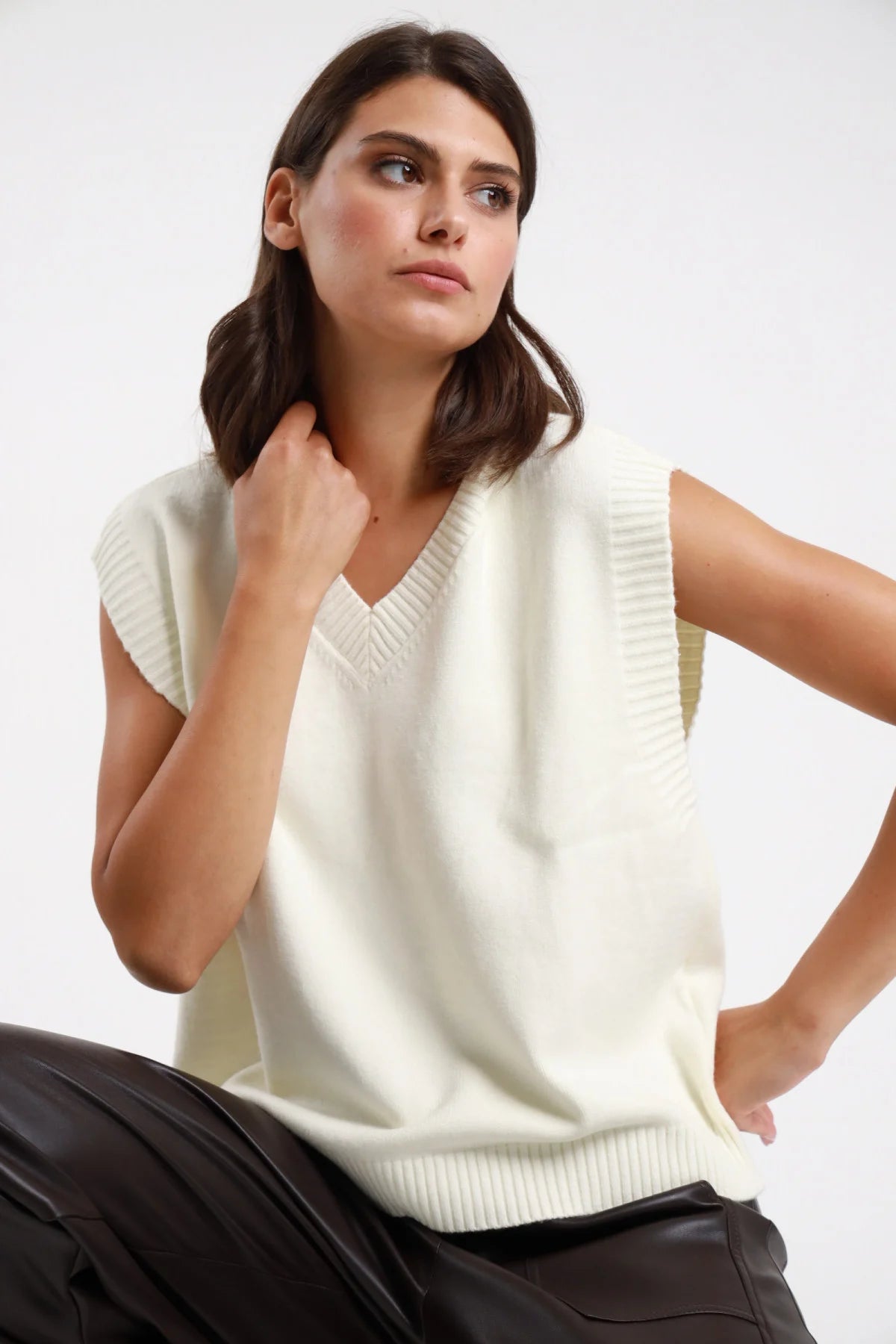 Gilet V maglia marrone cioccolato donna boxy cropped scollo V bordino costine cap-sleeve - vista frontale mezzo busto mano al collo con pantaloni ecopelle bordeaux