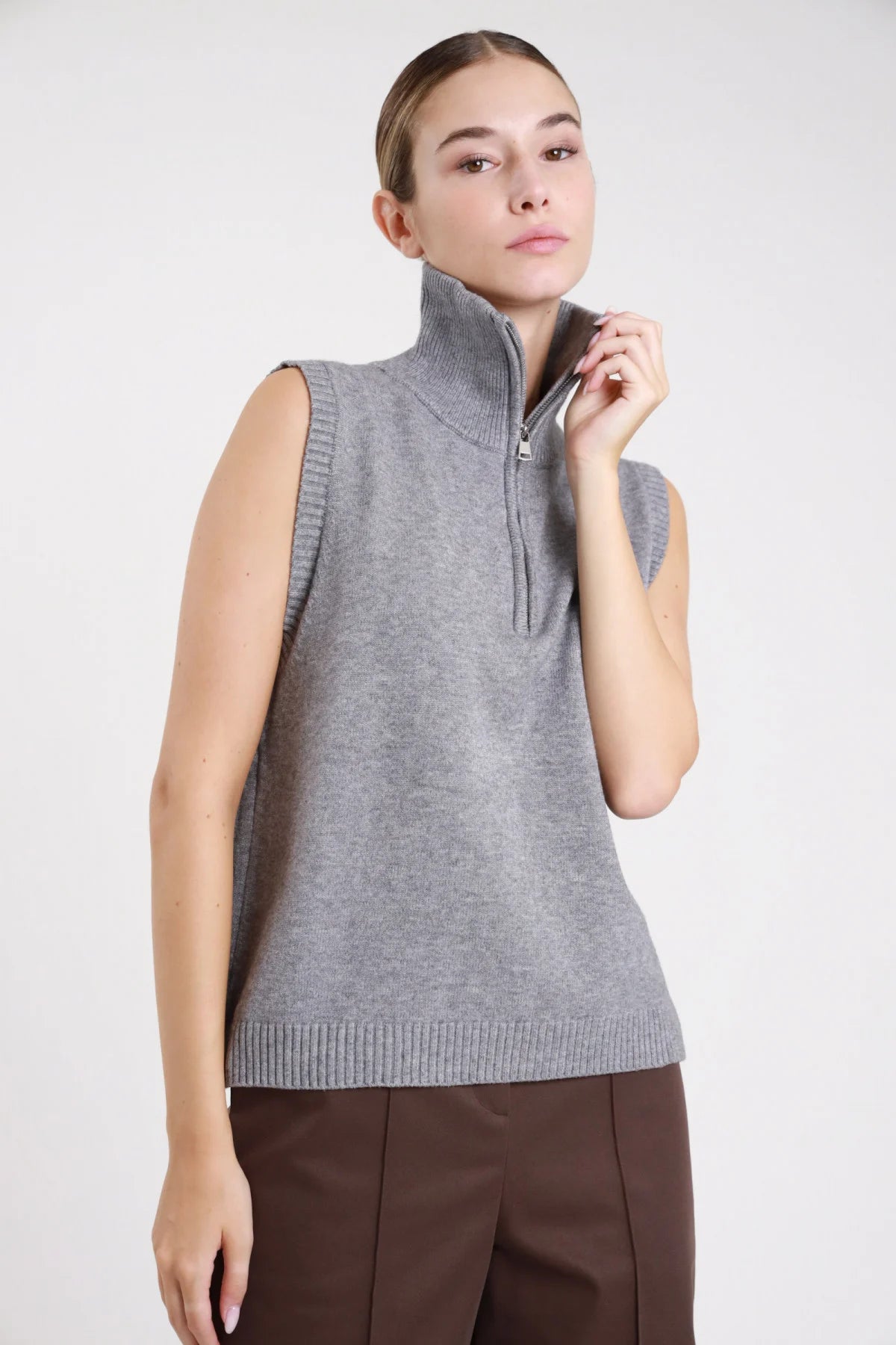 Gilet zip maglia grigio melange collo alto - modella busto tre quarti mano sulla zip sguardo frontale pantaloni marroni capelli raccolti